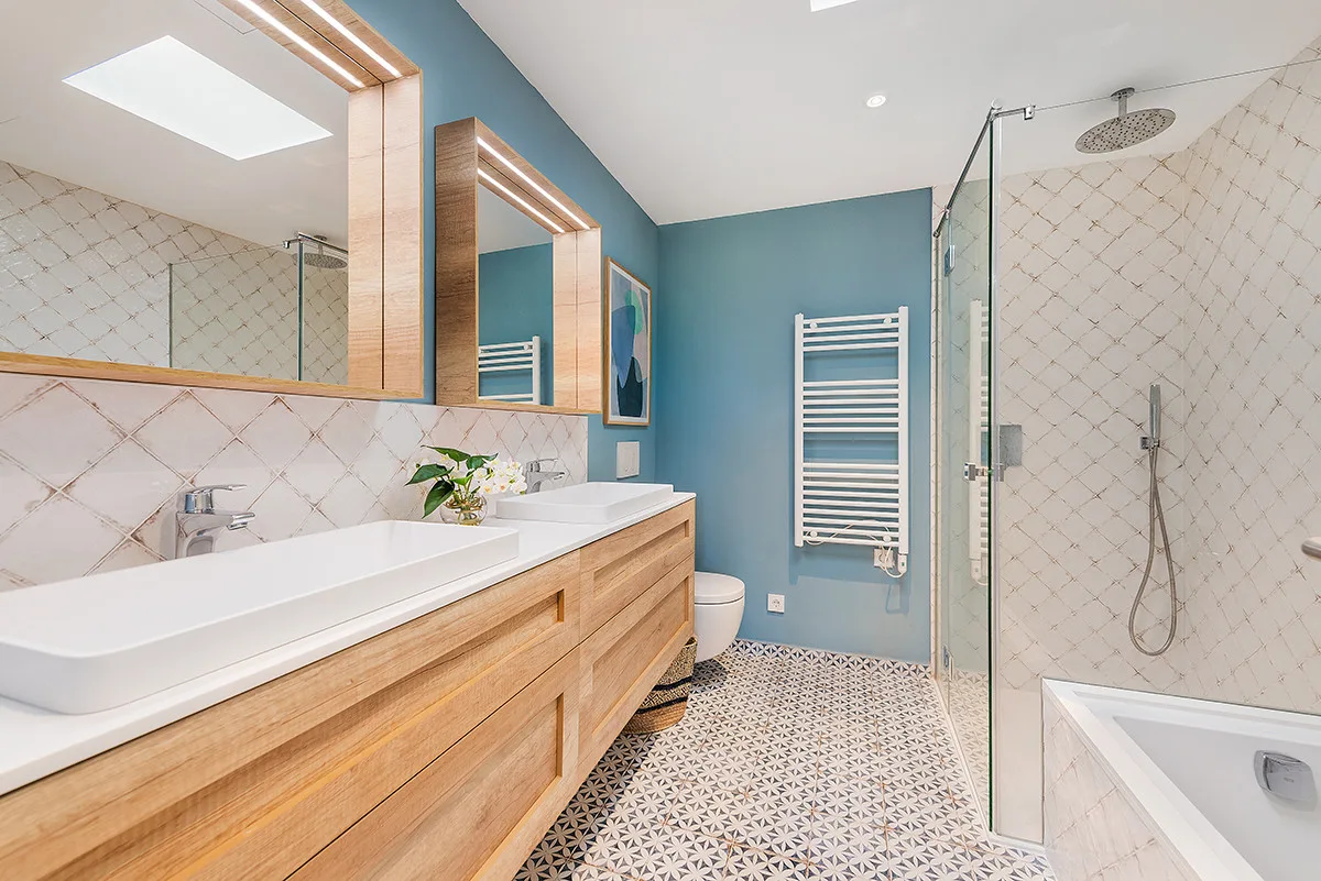 A bathroom with a long vanity, a wall-mounted towel warmer, and a glass shower.