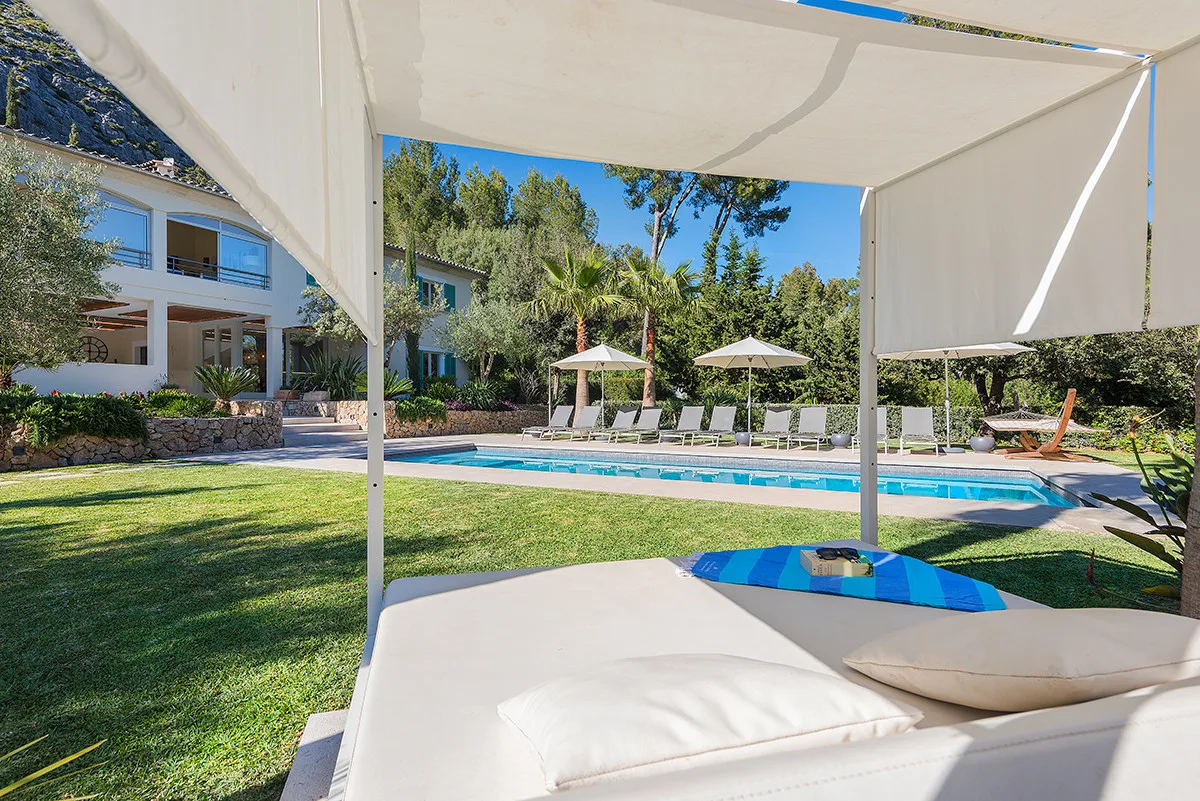 A shaded outdoor lounge overlooks a swimming pool and landscaped garden.