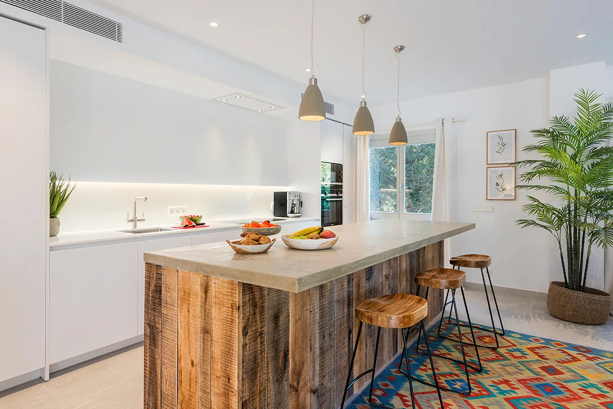 A bright kitchen with a long island, pendant lights, and stools.