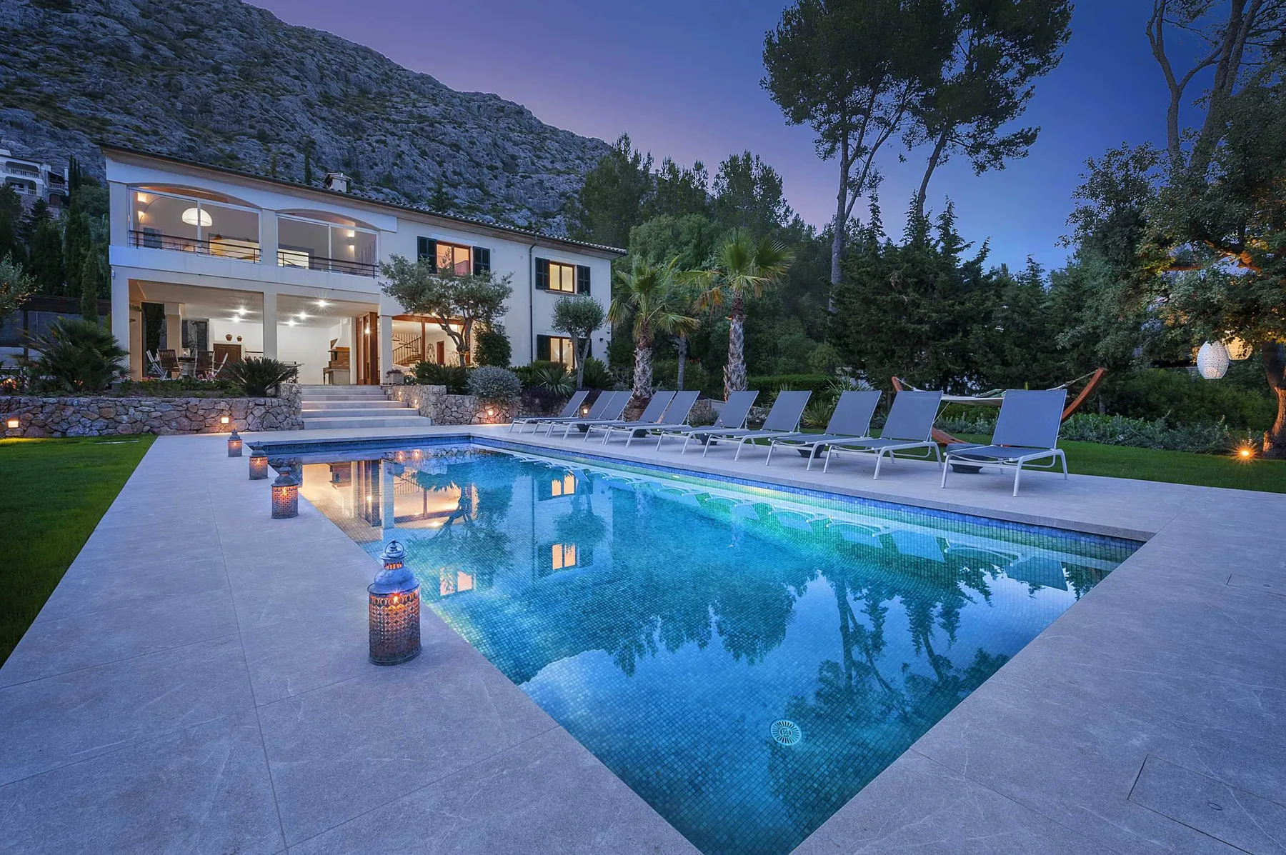 A swimming pool beside a modern house, with lounge seating along the edge.