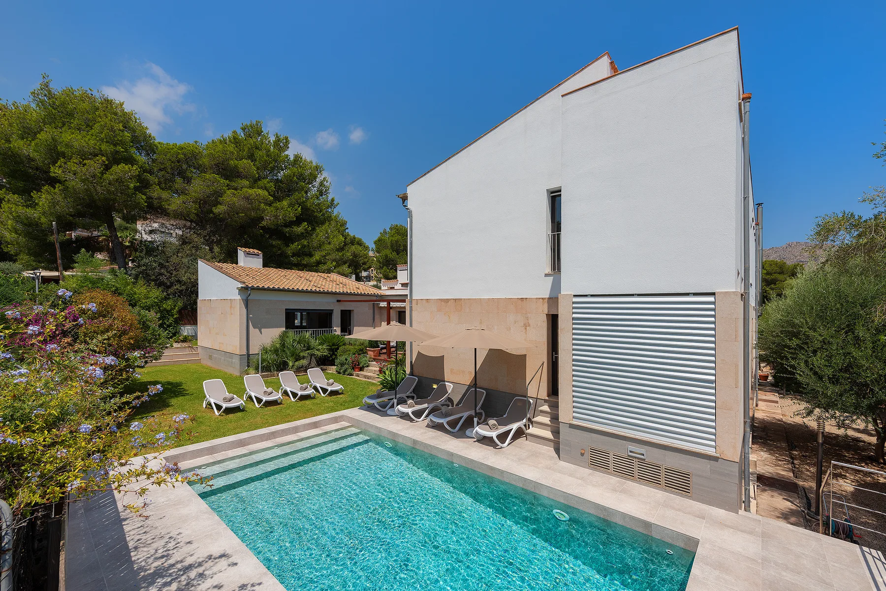 An outdoor swimming pool beside a white building and landscaped garden.
