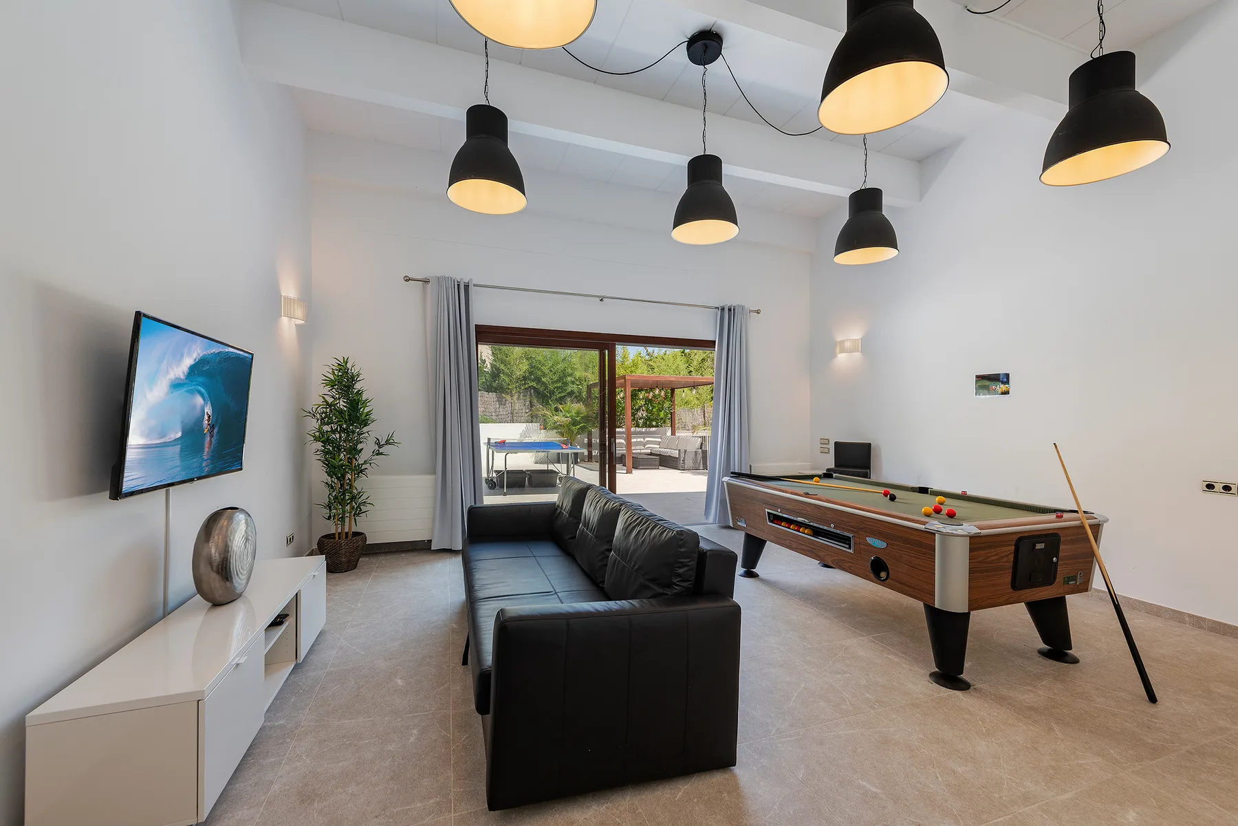 A bright recreation room with a pool table, seating, and sliding glass doors.