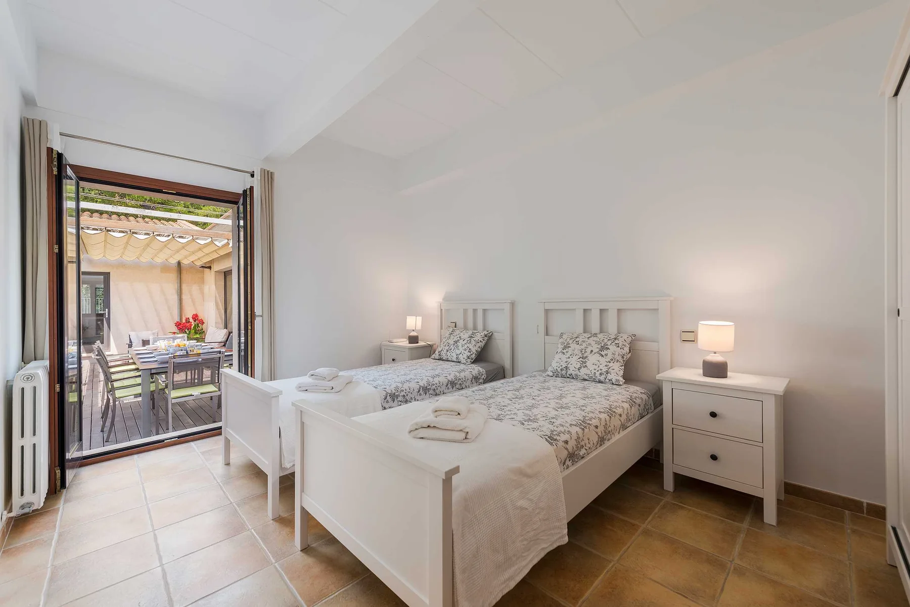 A bright bedroom with two beds and an open doorway to a patio.