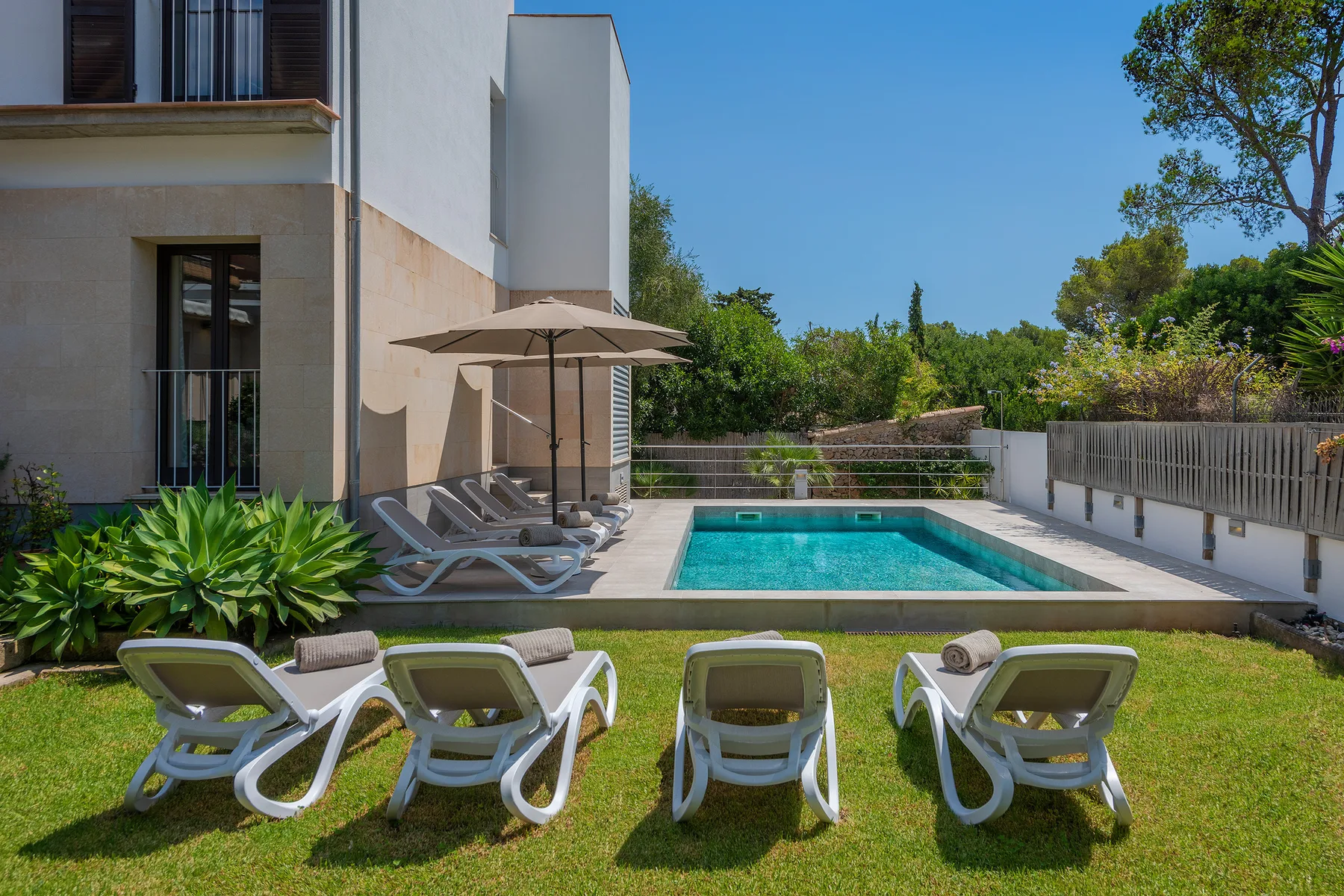 A rectangular swimming pool beside a modern house, with loungers arranged on the lawn.