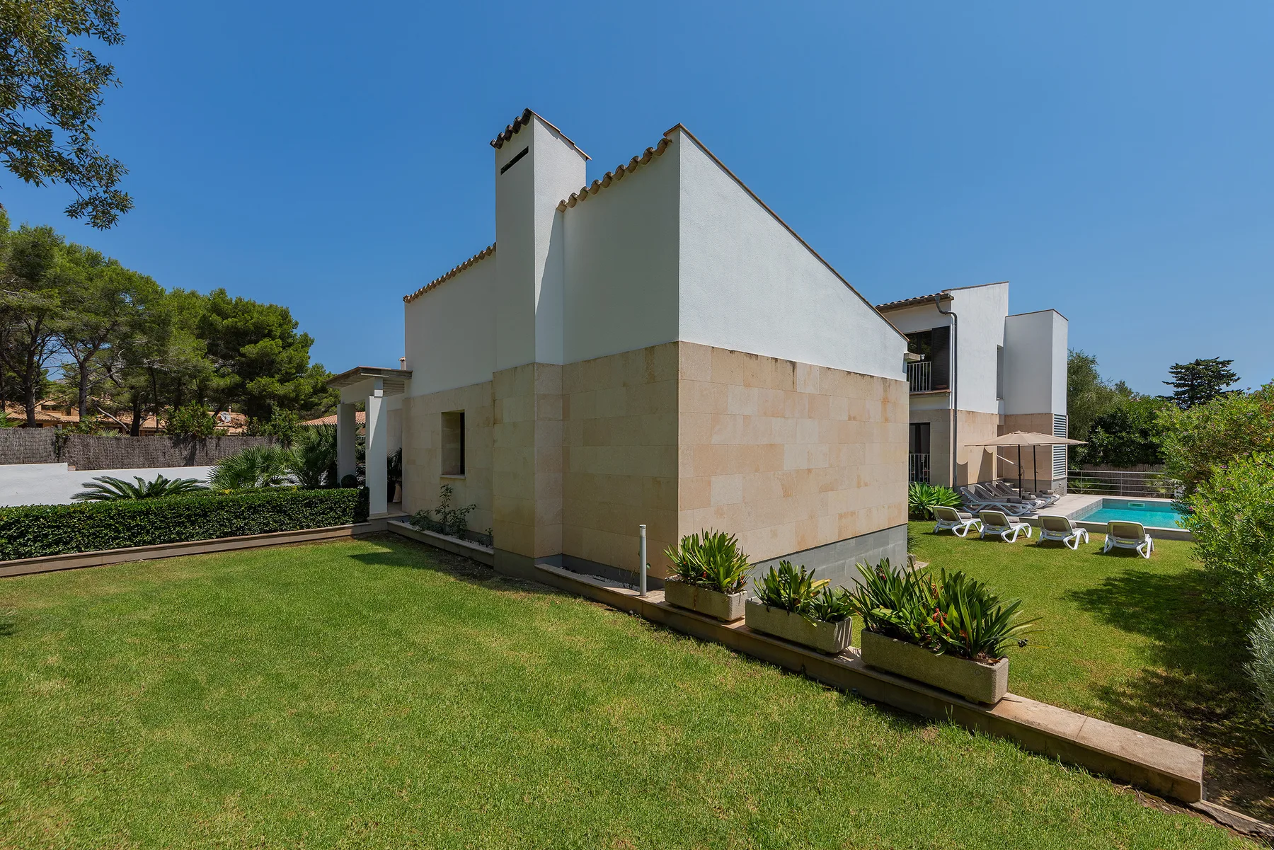 A modern house stands beside a lawn, with a swimming pool visible in the background.