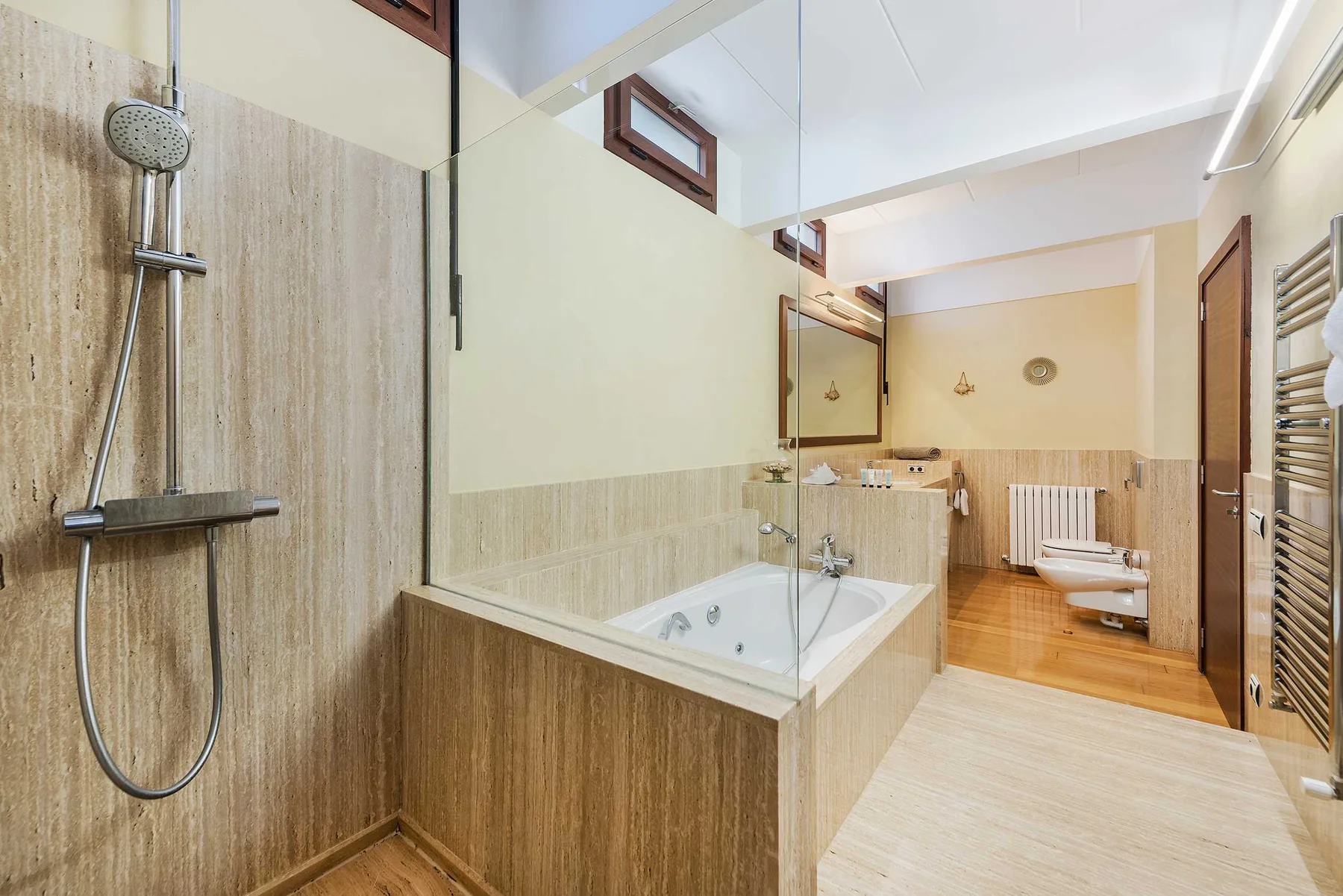 A bathroom with a bathtub, glass shower screen, and toilet.