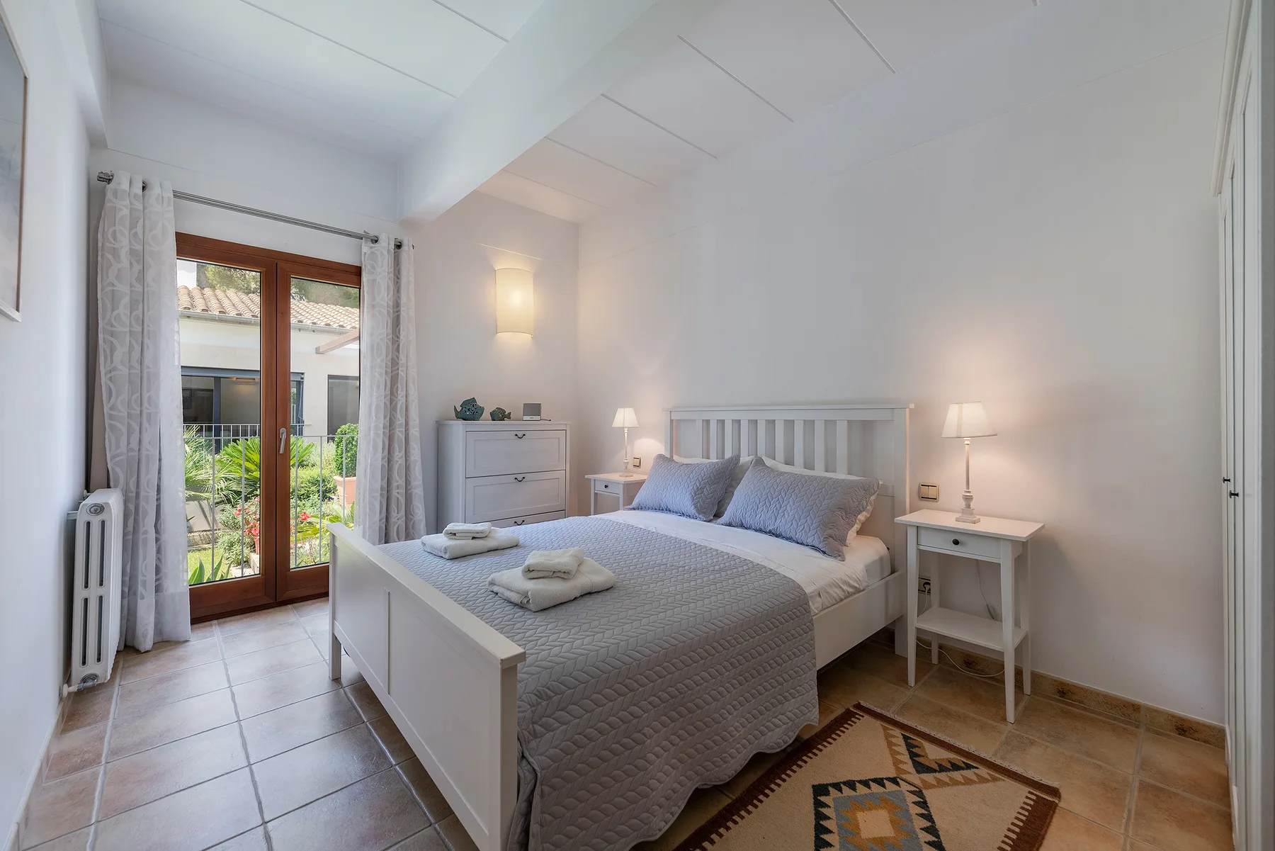 A bright bedroom with a double bed and glass doors opening to a garden.
