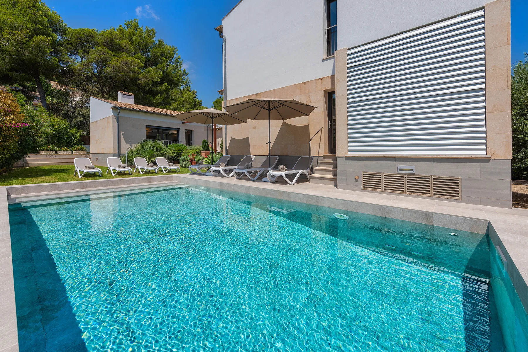 An outdoor swimming pool sits beside a modern building and poolside loungers.