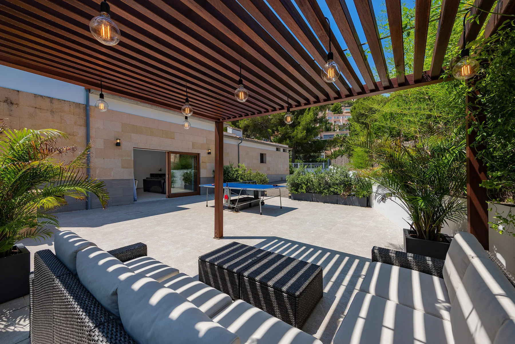 An outdoor patio with cushioned seating beneath a slatted pergola.