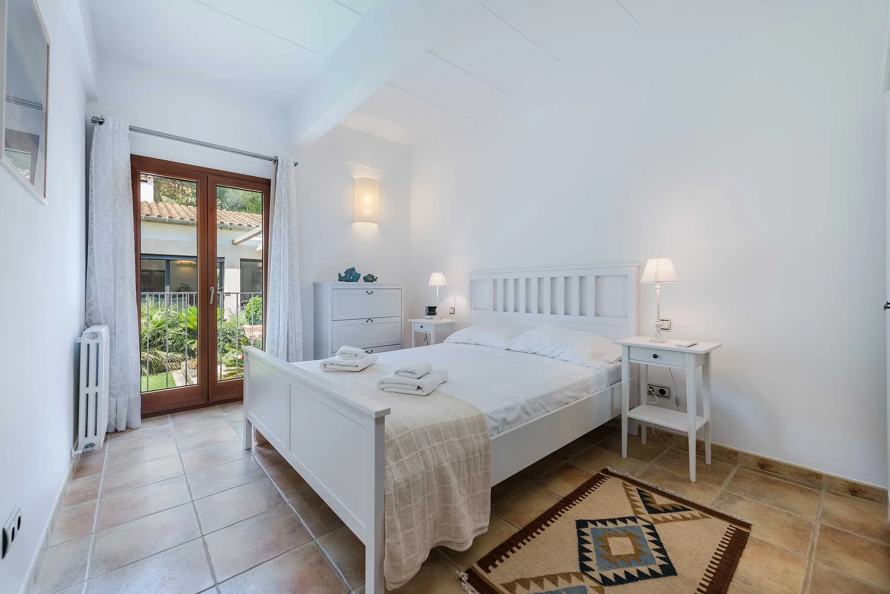 A bright bedroom with a double bed, bedside table, and glass doors opening to a patio.