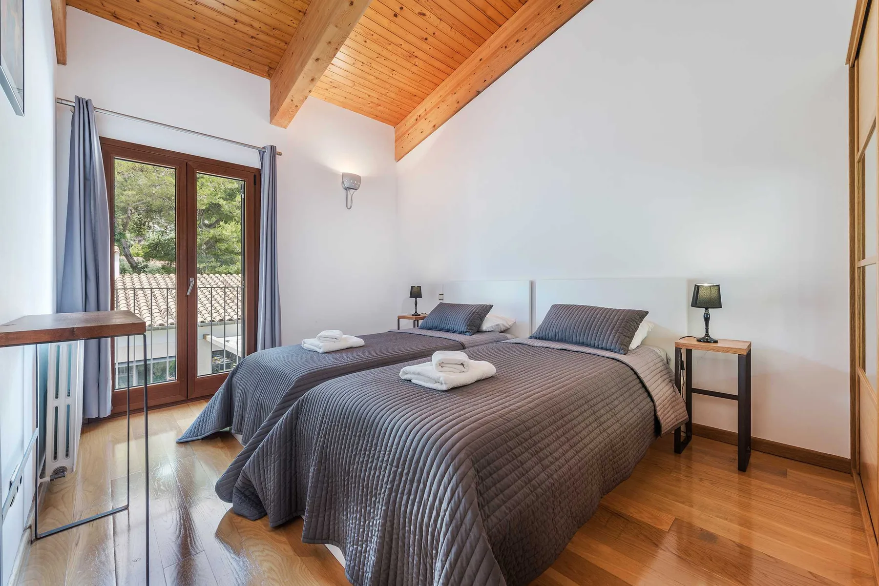 A bedroom with a large bed, bedside tables, and glass doors opening to a balcony.