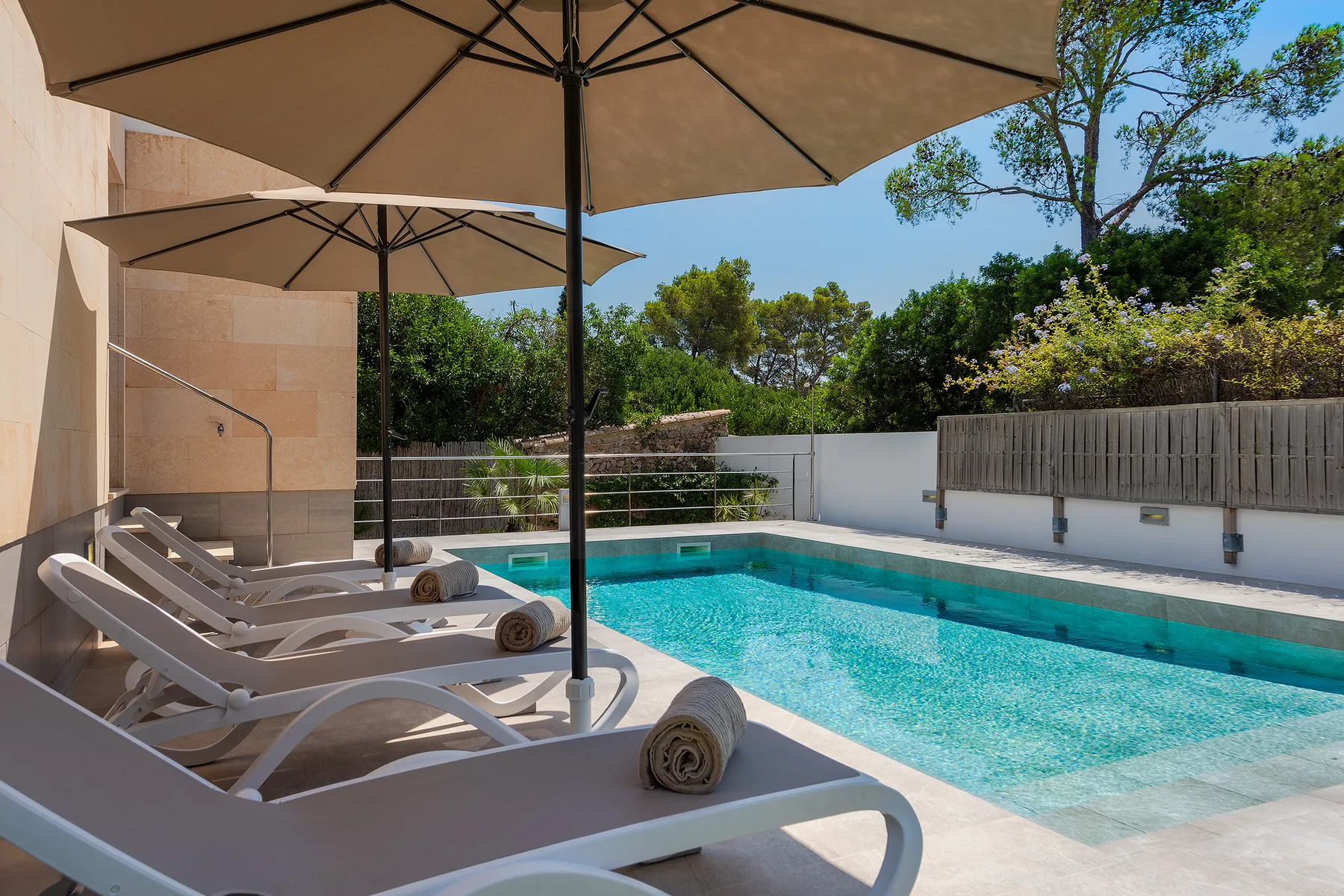 An outdoor swimming pool beside sun loungers shaded by large umbrellas.