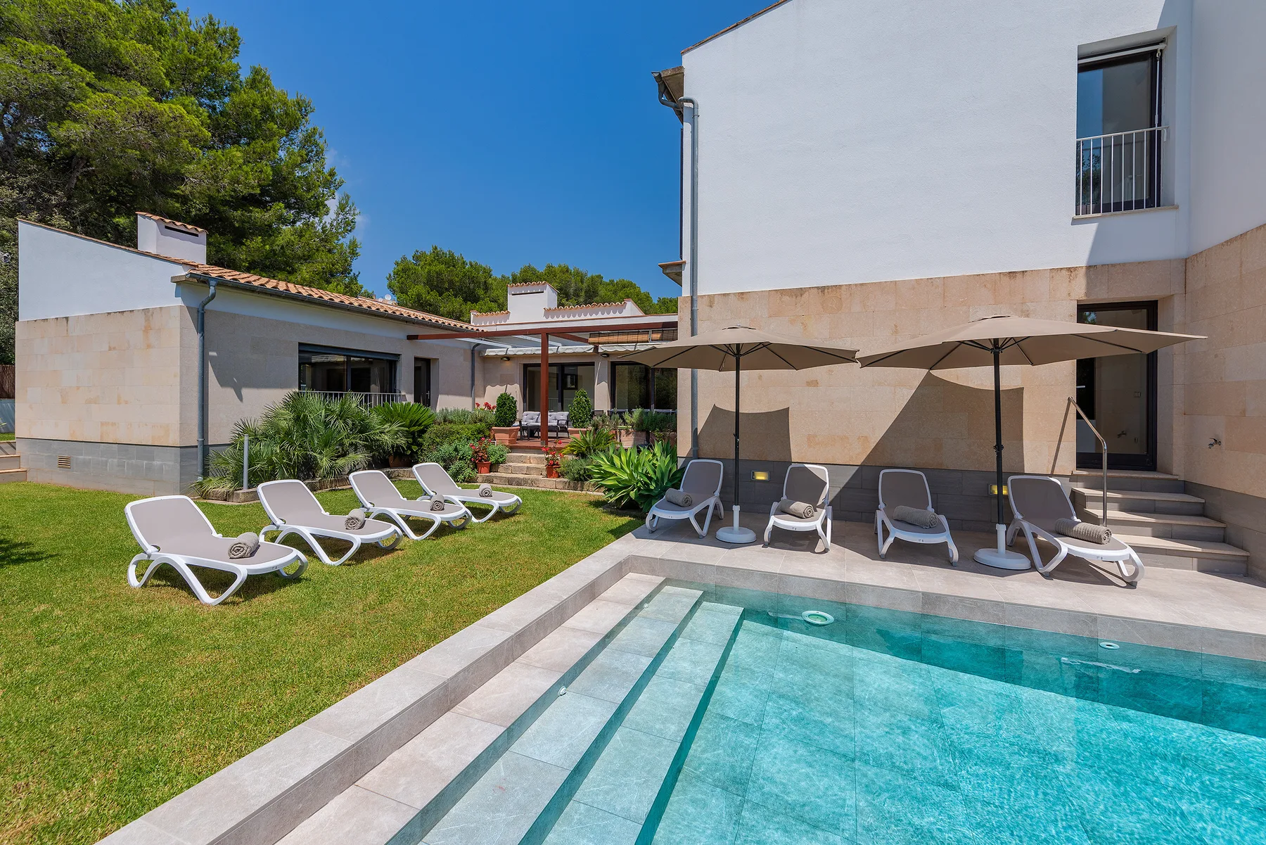 An outdoor pool beside a lawn with loungers and shaded seating.