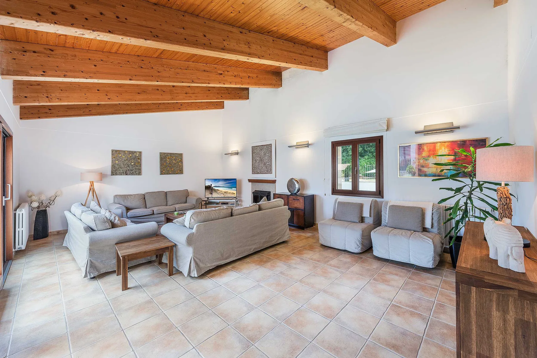 A bright living room with seating arranged around a low coffee table beneath a timber ceiling.