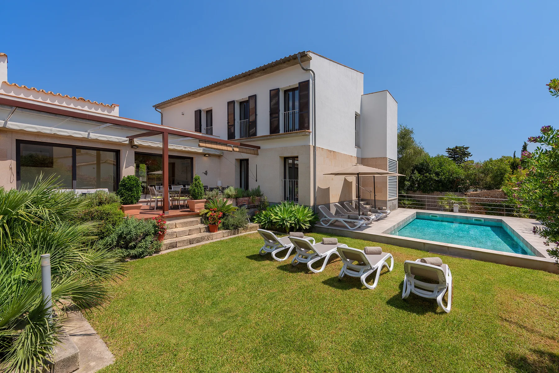 A modern house and outdoor swimming pool sit beside a lawn with loungers.