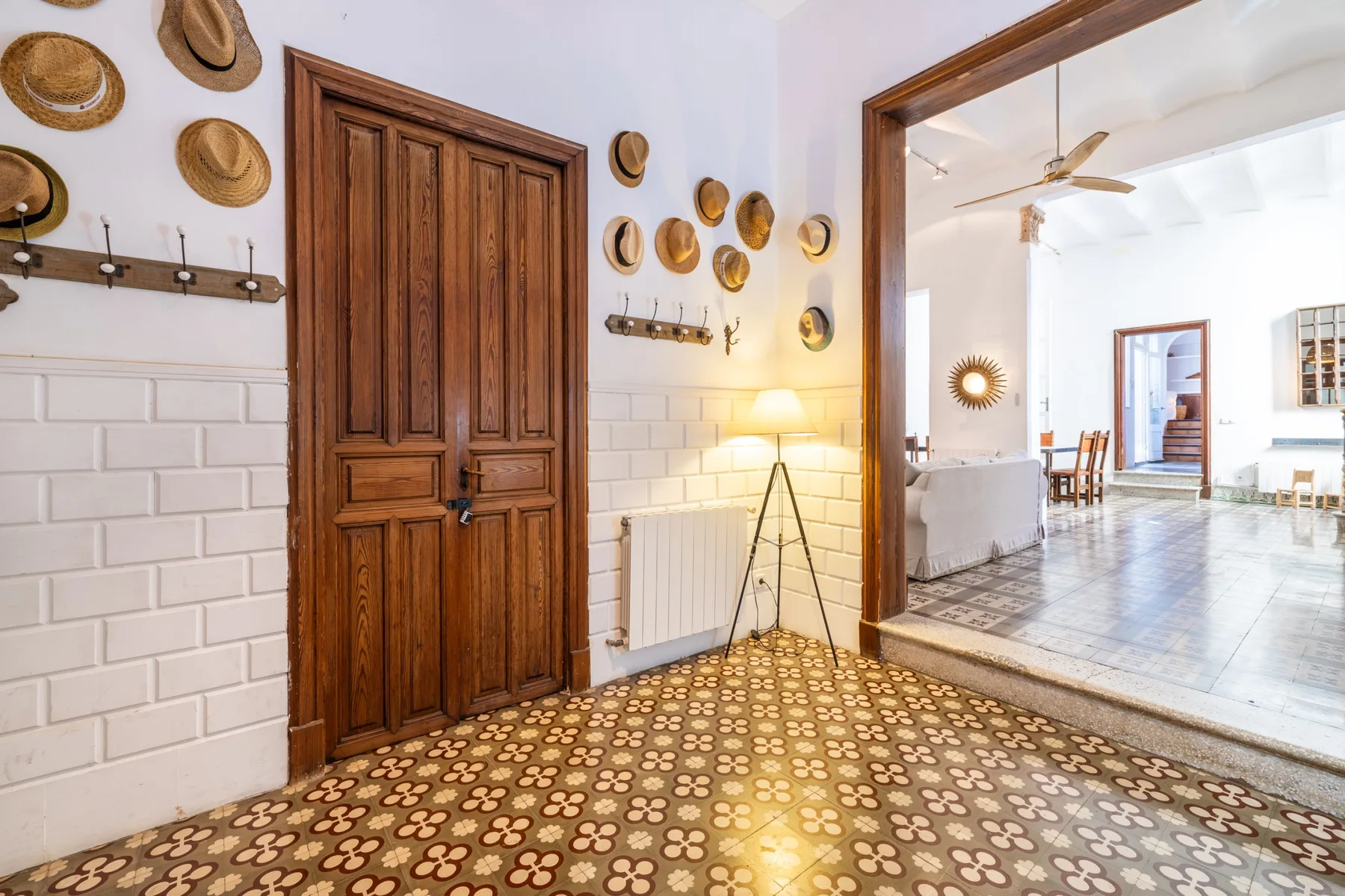 Un recibidor con suelo de baldosas, una puerta de madera y acceso a una sala luminosa.