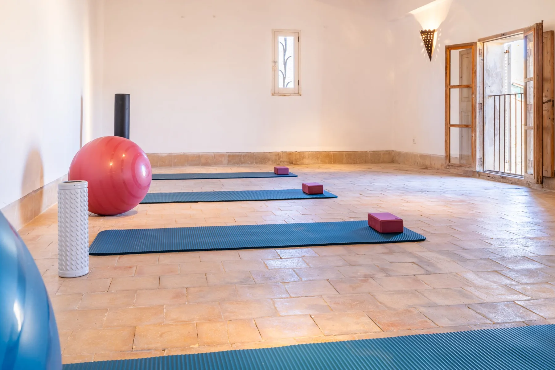 Una sala de ejercicios con esterillas y pelotas sobre un suelo de baldosas.