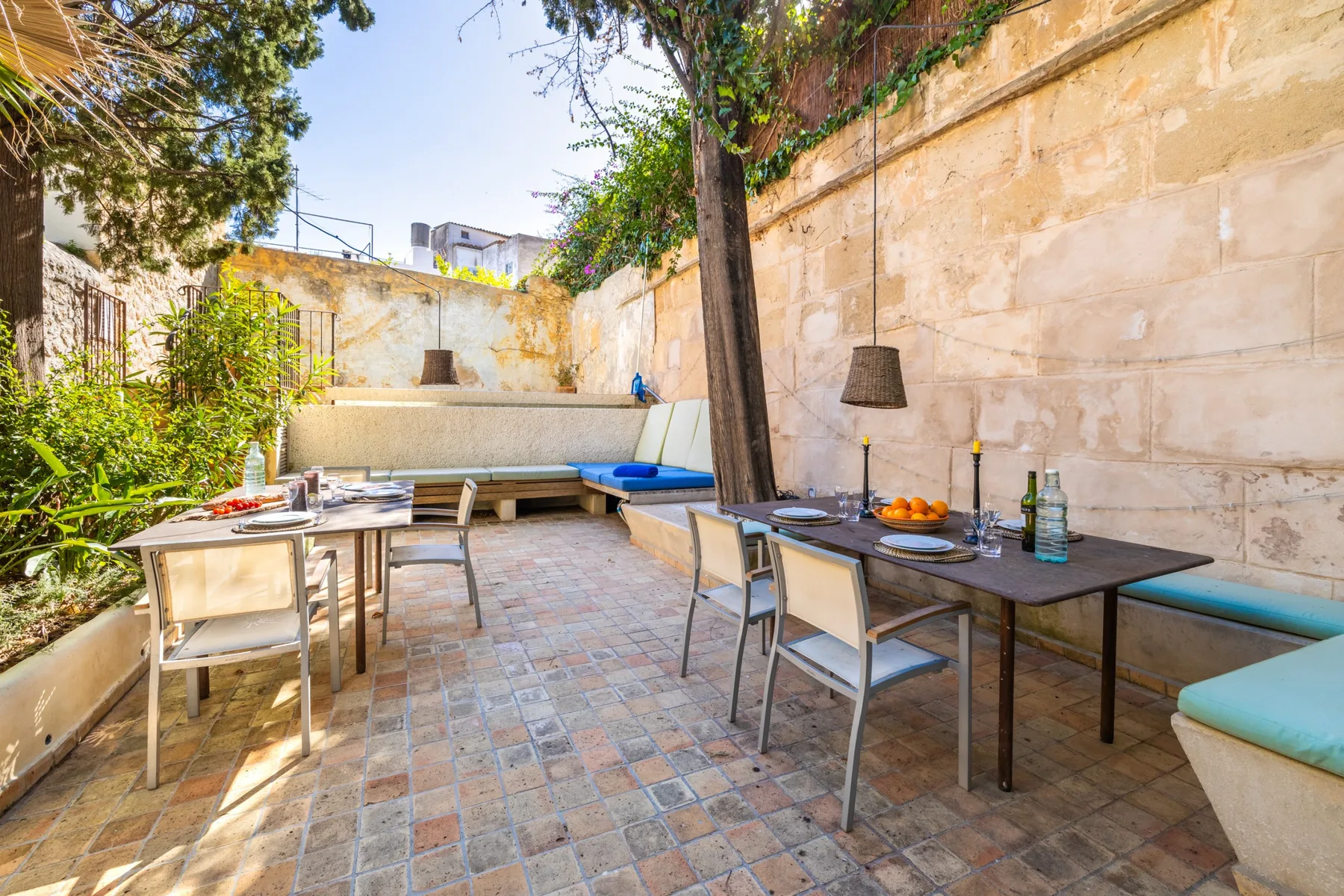 Un patio comedor al aire libre con mesas y asientos junto a un jardín frondoso.