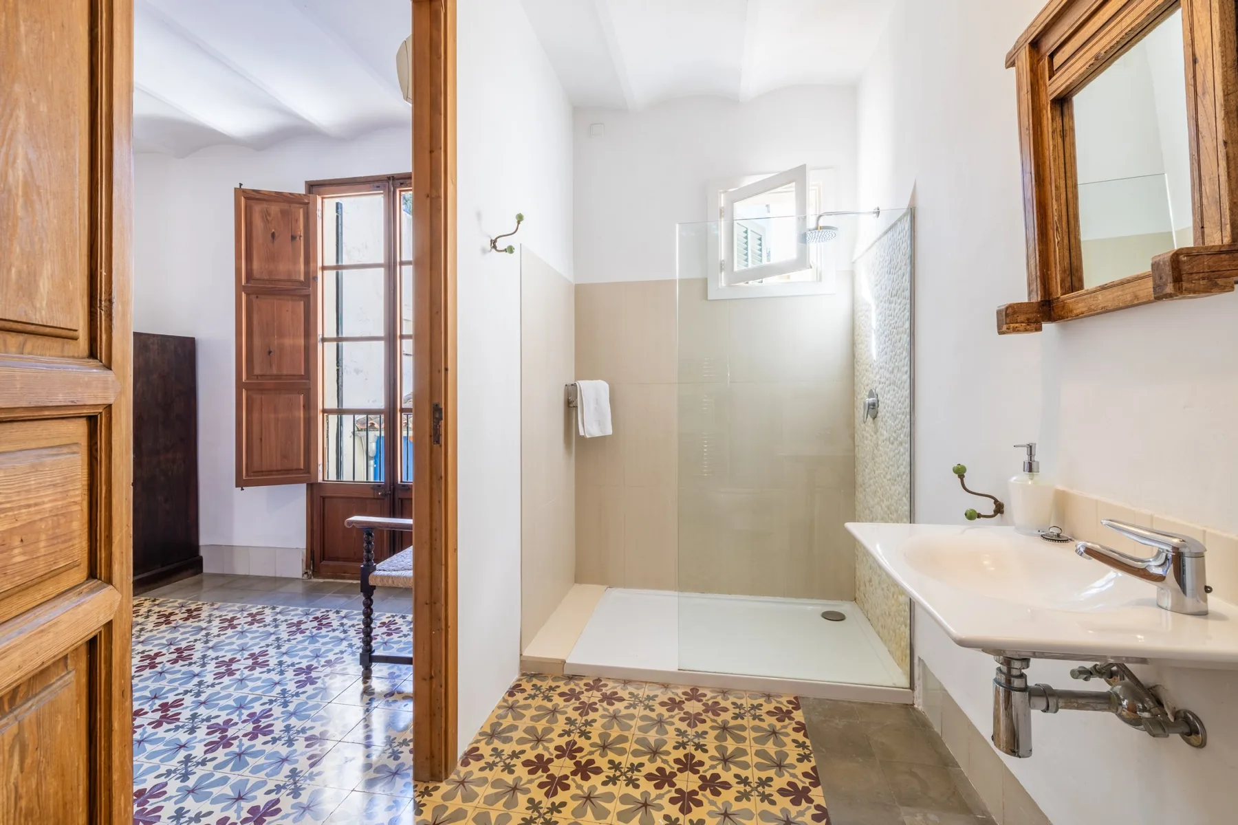 Un baño con ducha y lavabo junto a un espejo con marco de madera.