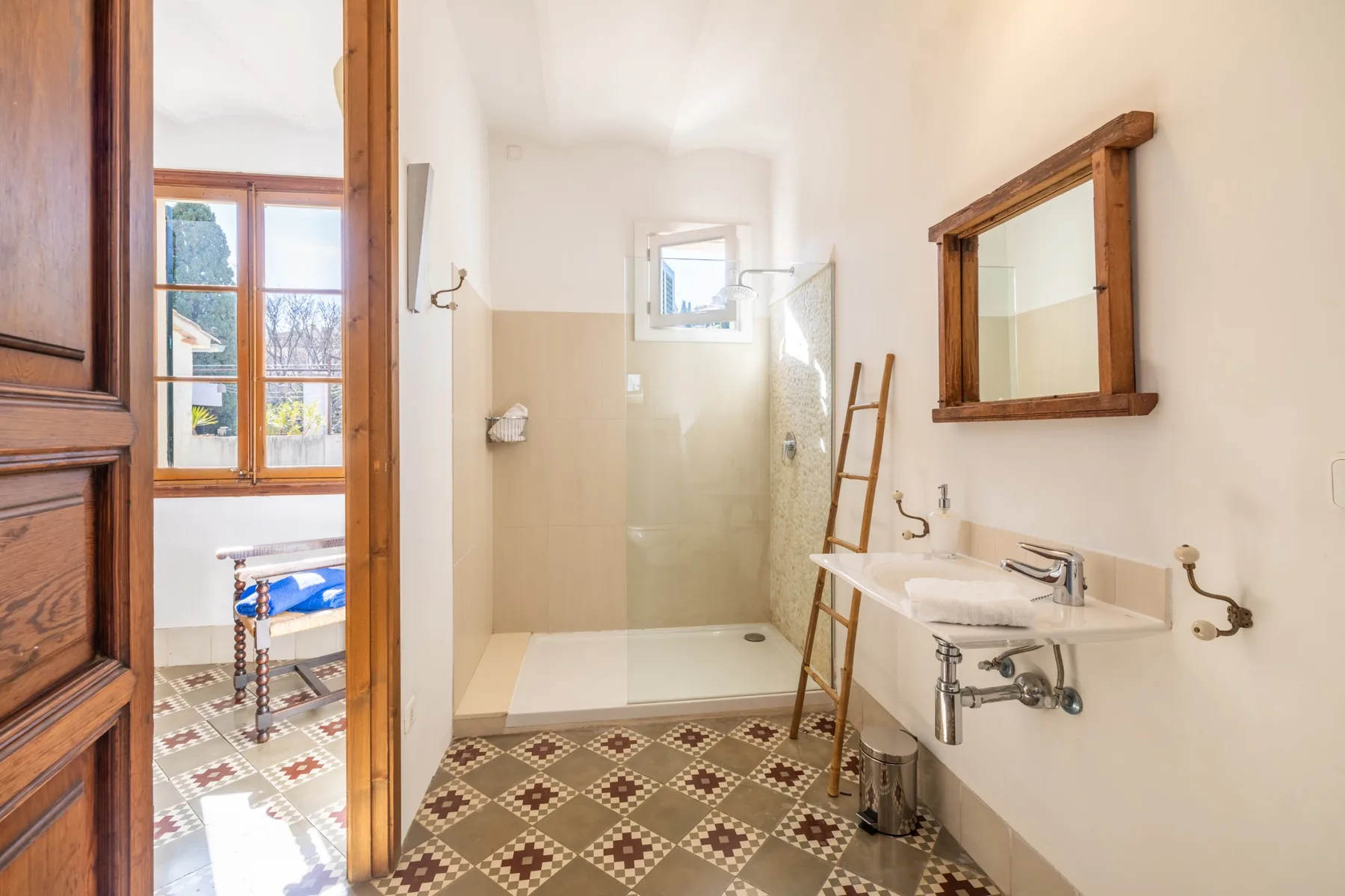 Un baño con ducha de vidrio, lavabo y suelo de baldosas estampadas.