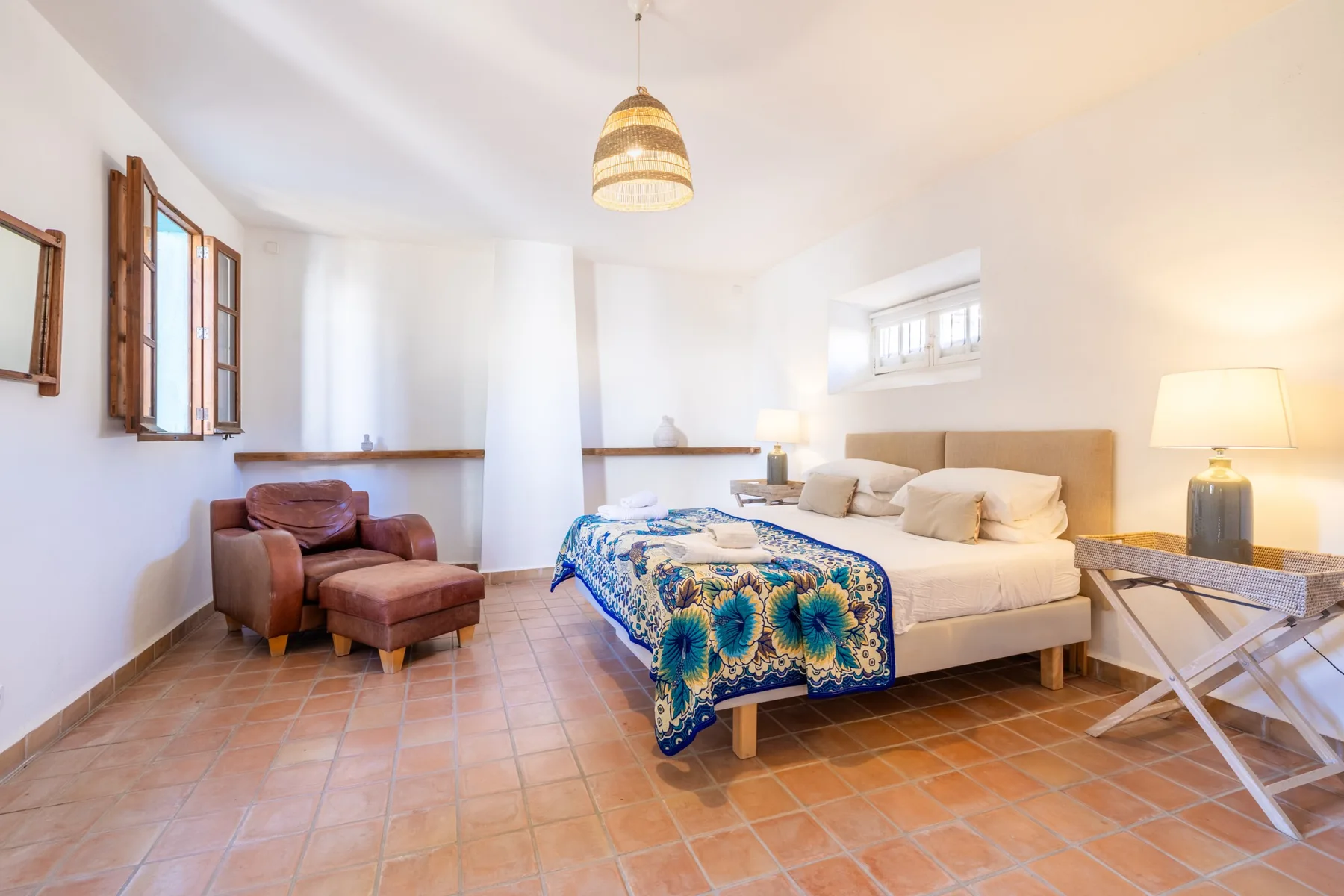 Un dormitorio luminoso con una cama doble, una colcha colorida y un sillón.