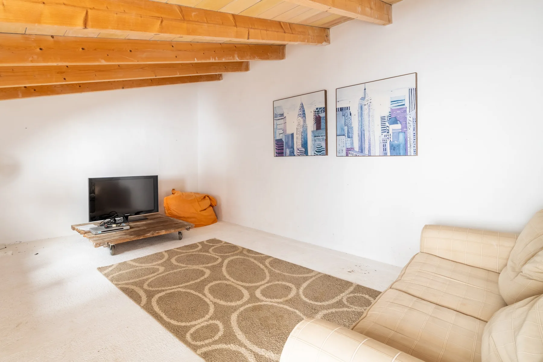 Una sala luminosa con televisor, asientos beige y una alfombra estampada.