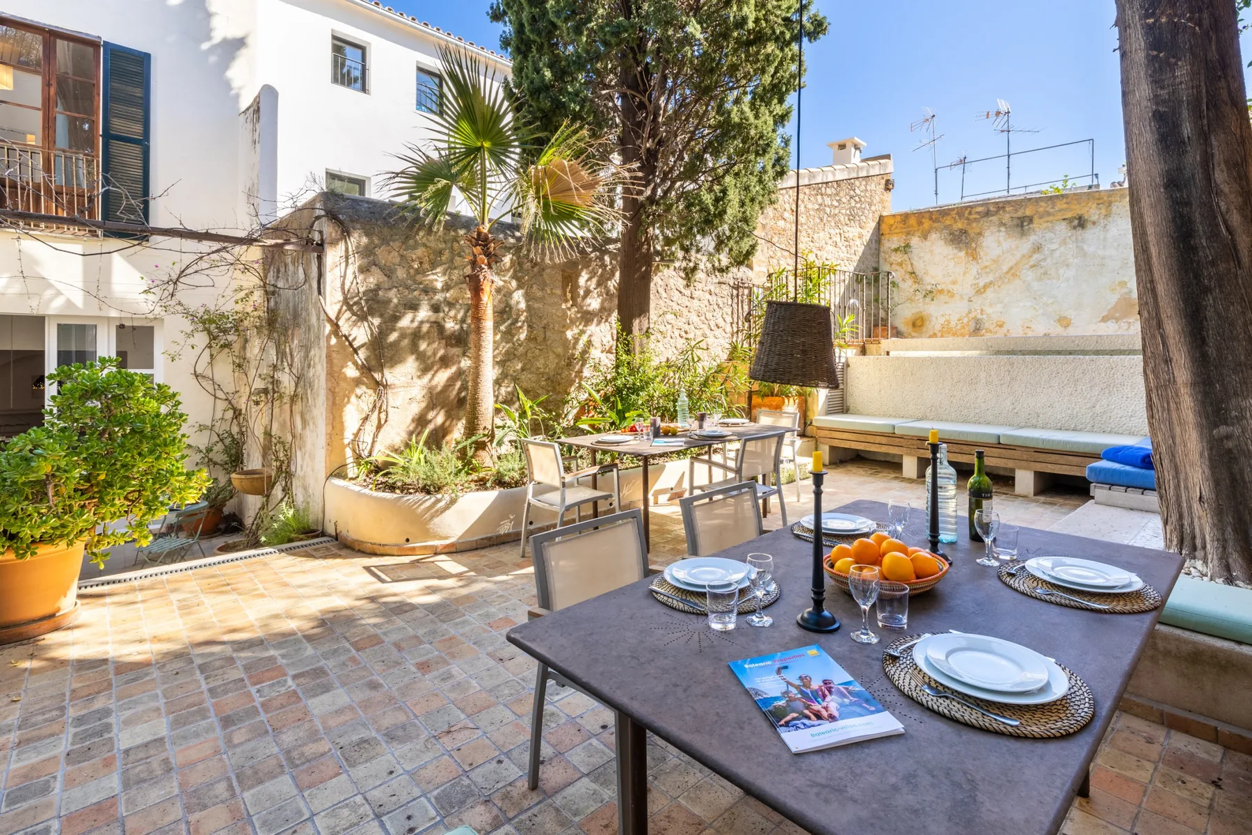 Un patio soleado con una mesa de comedor, asientos y plantas en macetas.