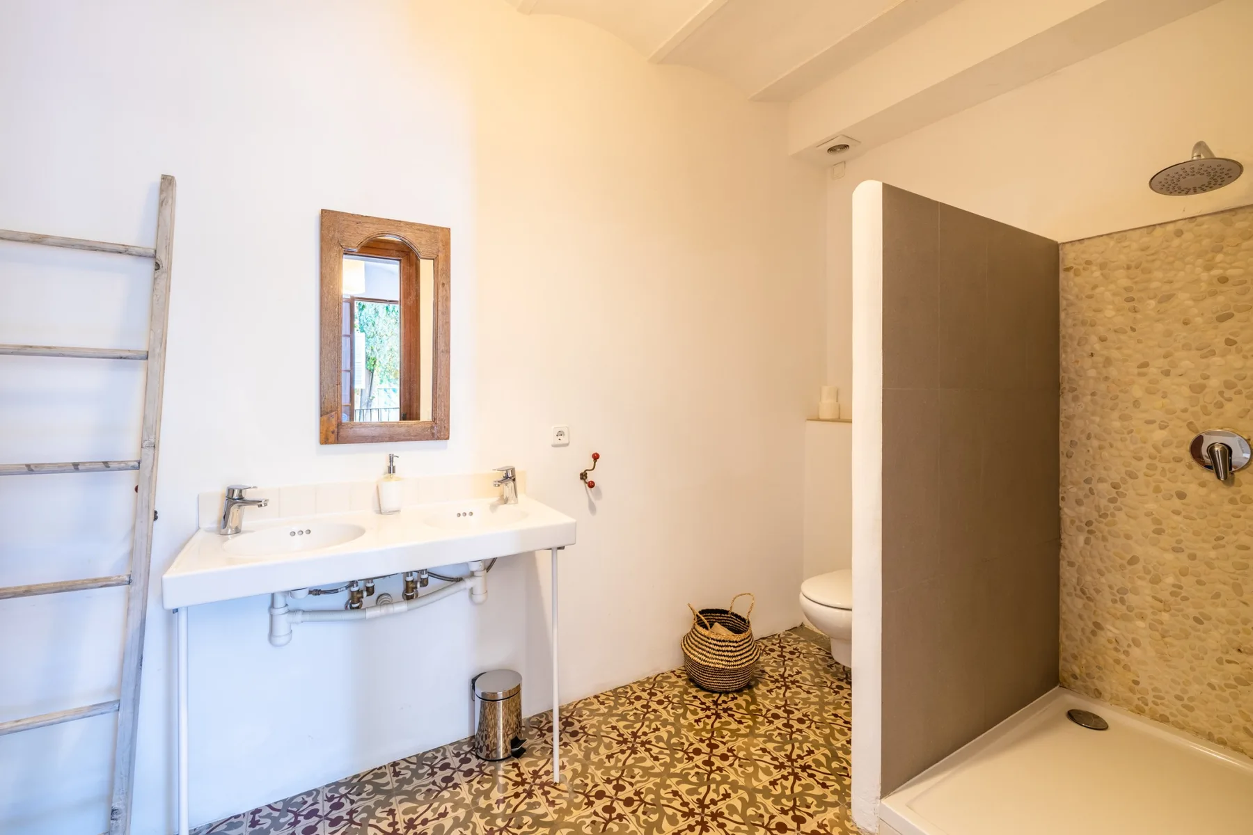 Un baño con lavabo de pared, espejo y zona de ducha abierta.
