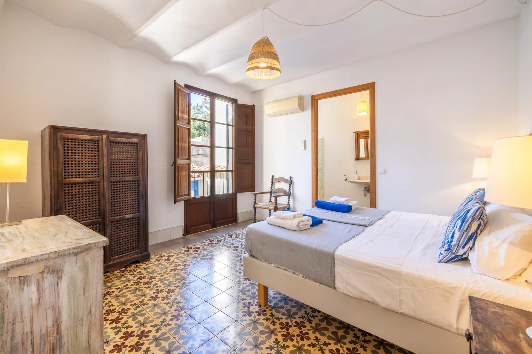 Un dormitorio con una cama, suelo de baldosas estampadas y contraventanas de madera abiertas.