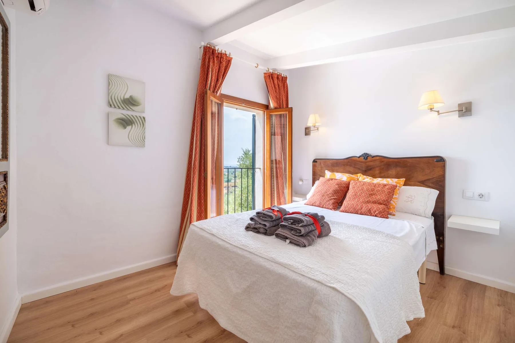 A bedroom with a neatly made bed and orange curtains beside a glass door.