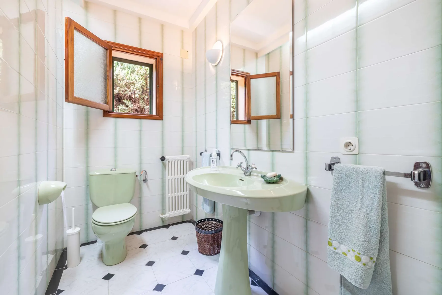 A tiled bathroom with a pedestal sink, toilet, and window.