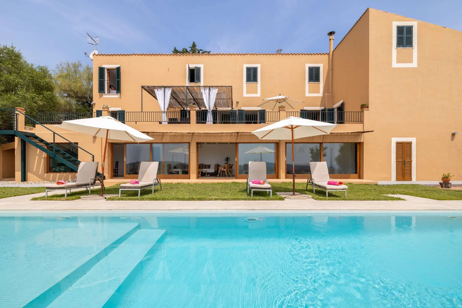 A swimming pool sits in front of a two-story building with a terrace.