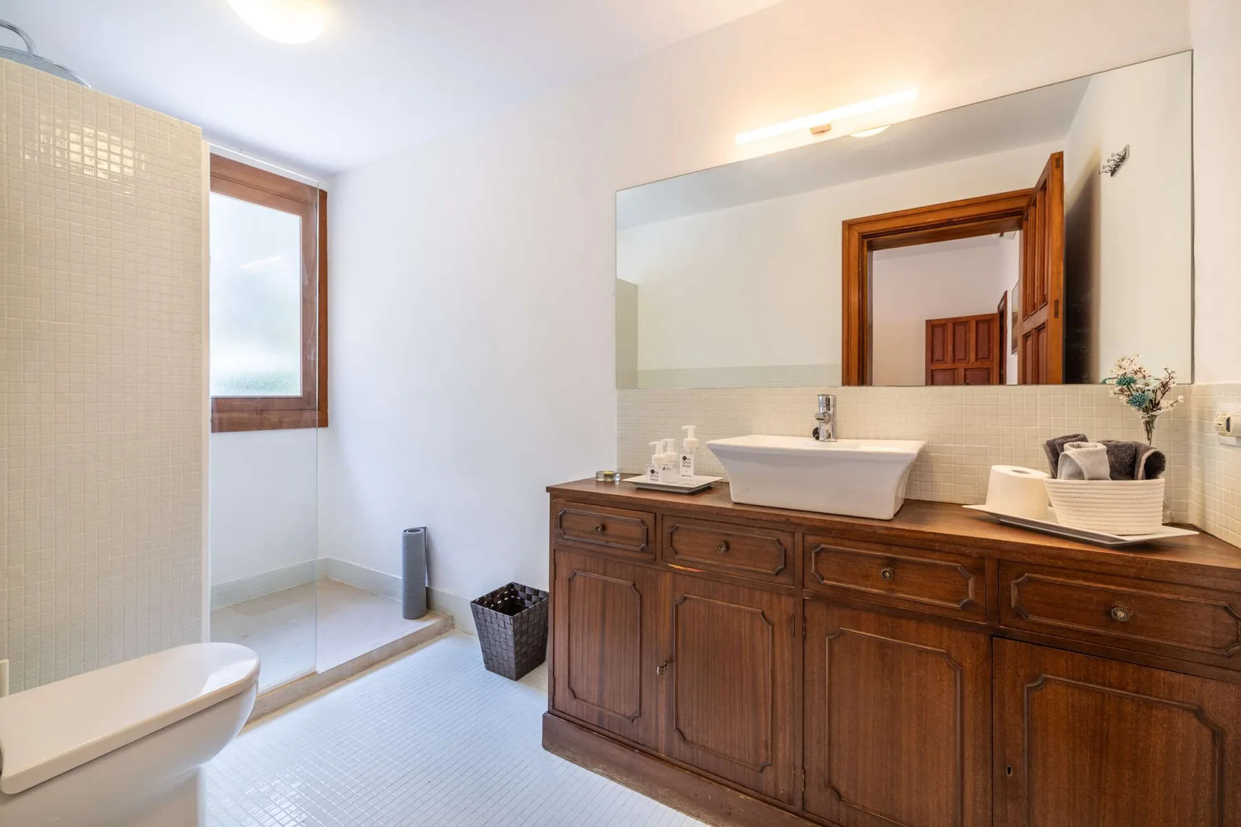 A bathroom with a long wooden vanity, sink, and walk-in shower.