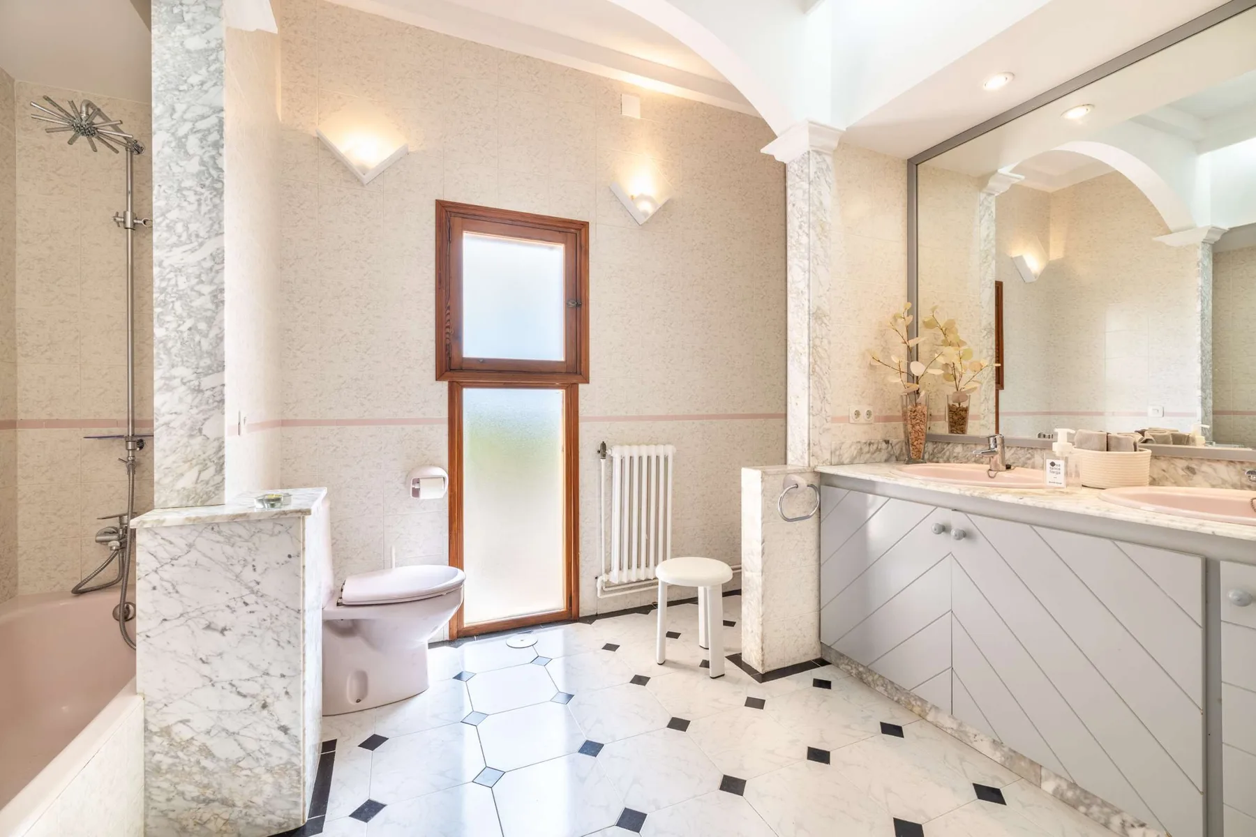 A bright bathroom with a bathtub, toilet, and a wide vanity.
