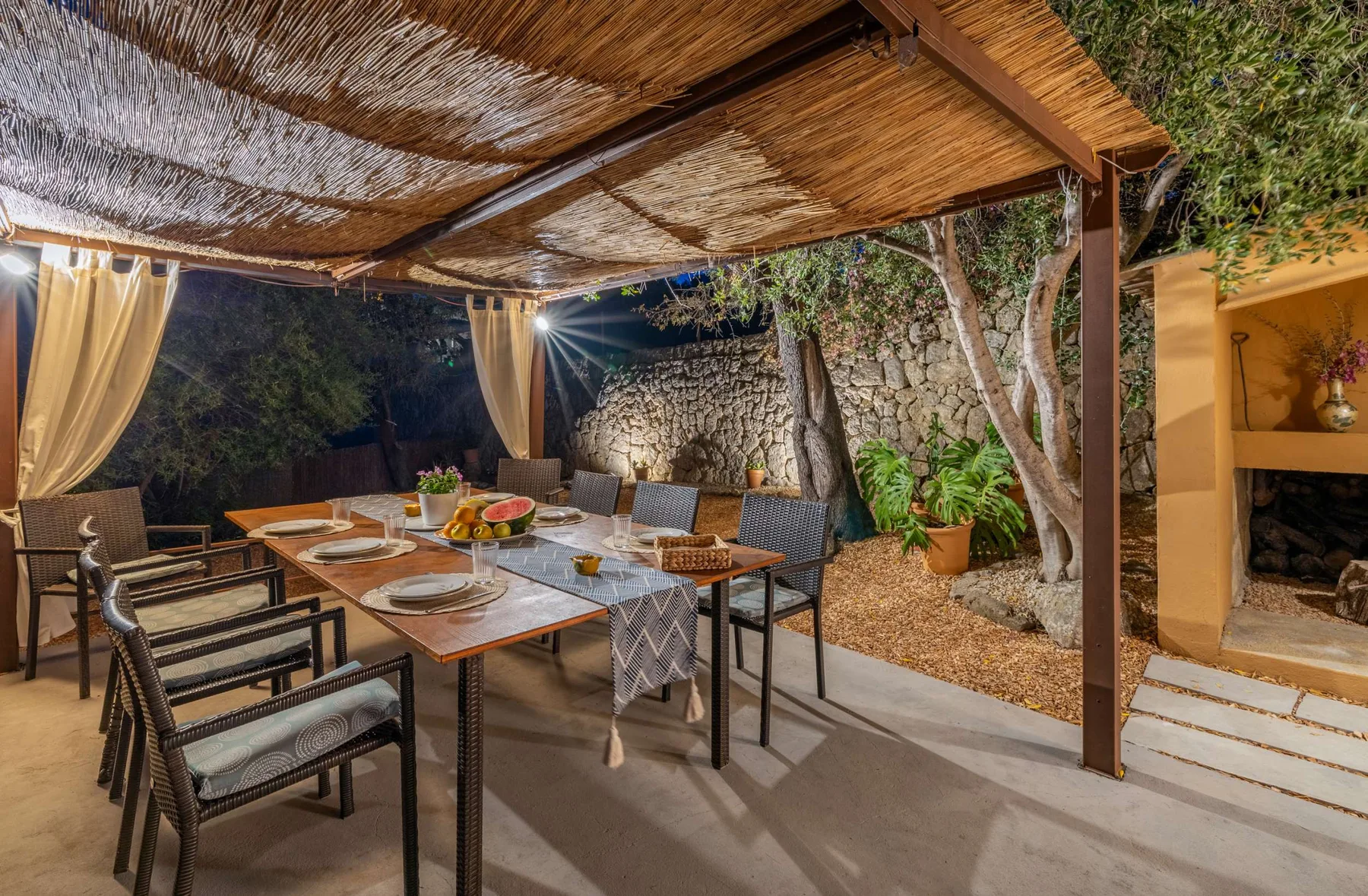 A covered outdoor dining area with a long table and surrounding seating.