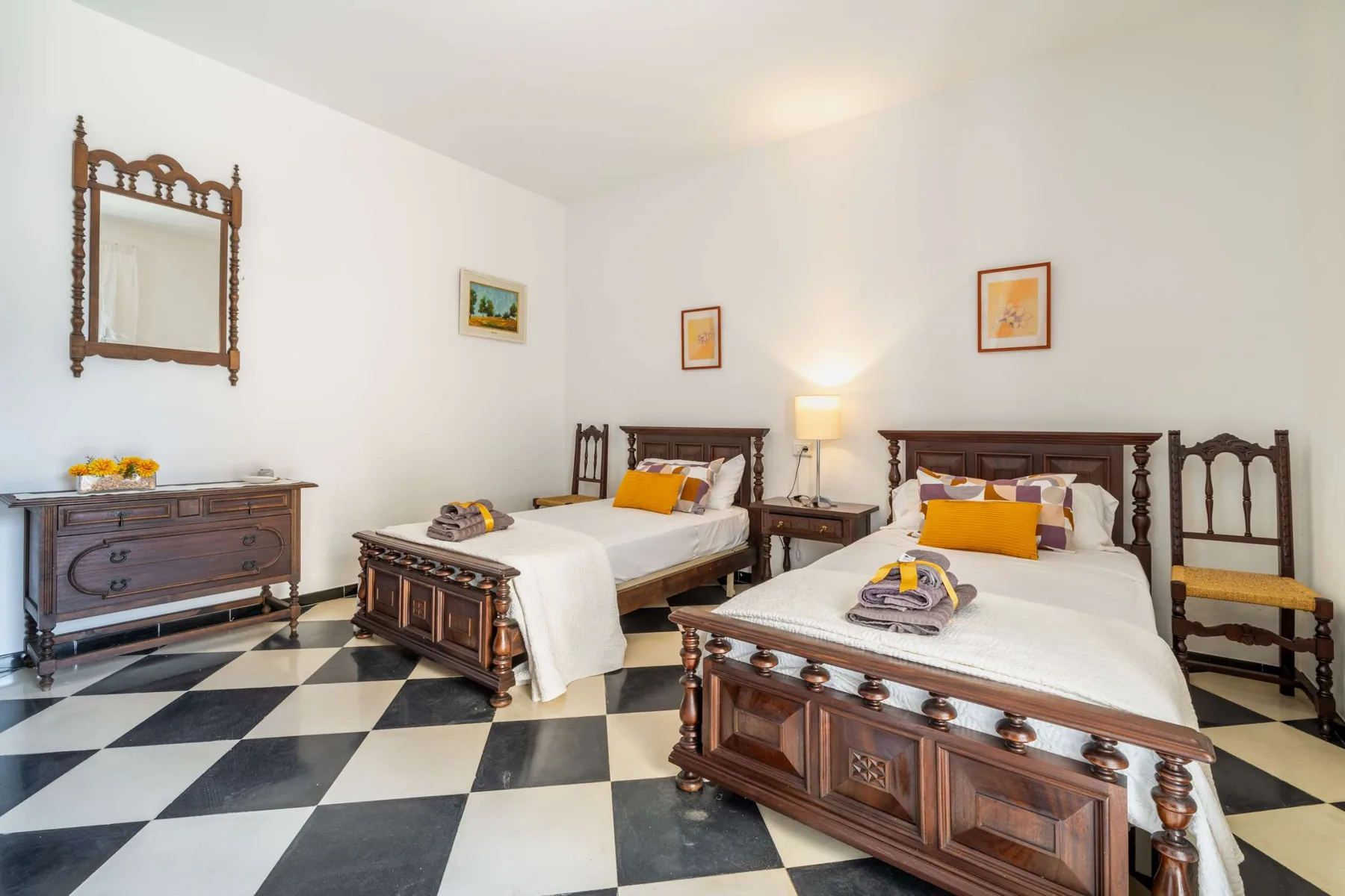 A bedroom with two beds, dark wood furniture, and a checkered tile floor.