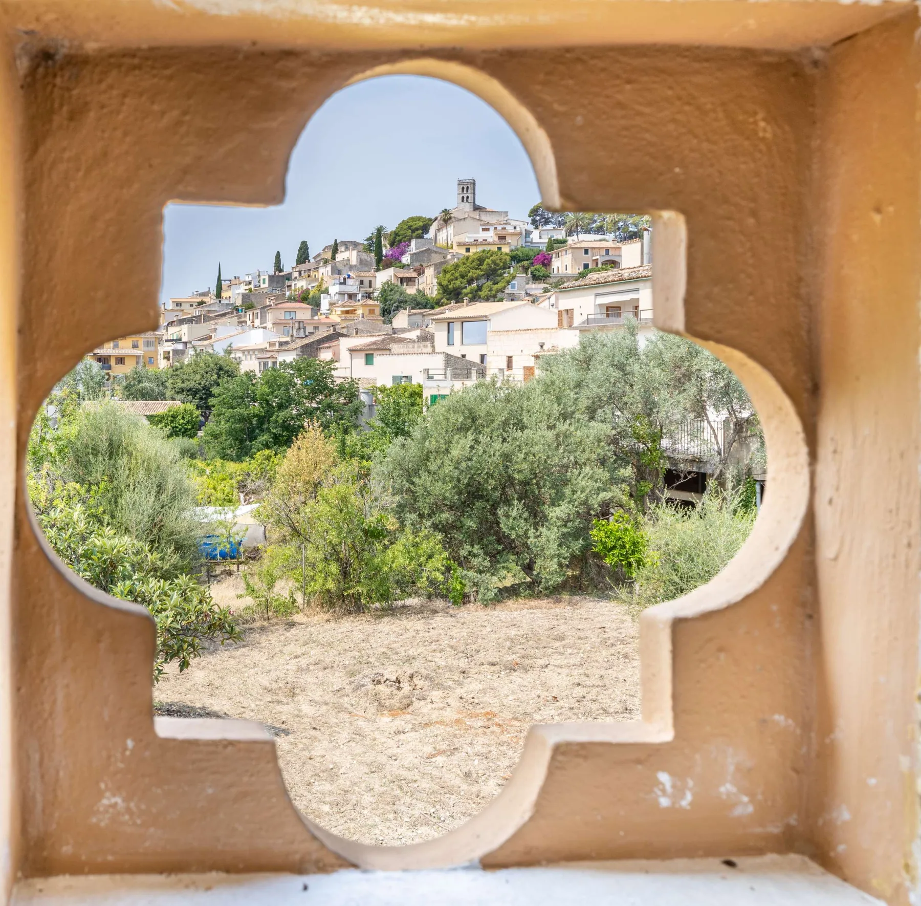 A hillside village with clustered buildings and greenery is seen through a decorative opening.