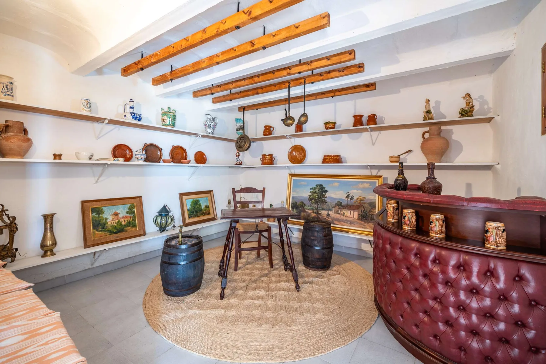 A rustic dining area features a wooden table, decorative pottery, and exposed ceiling beams.