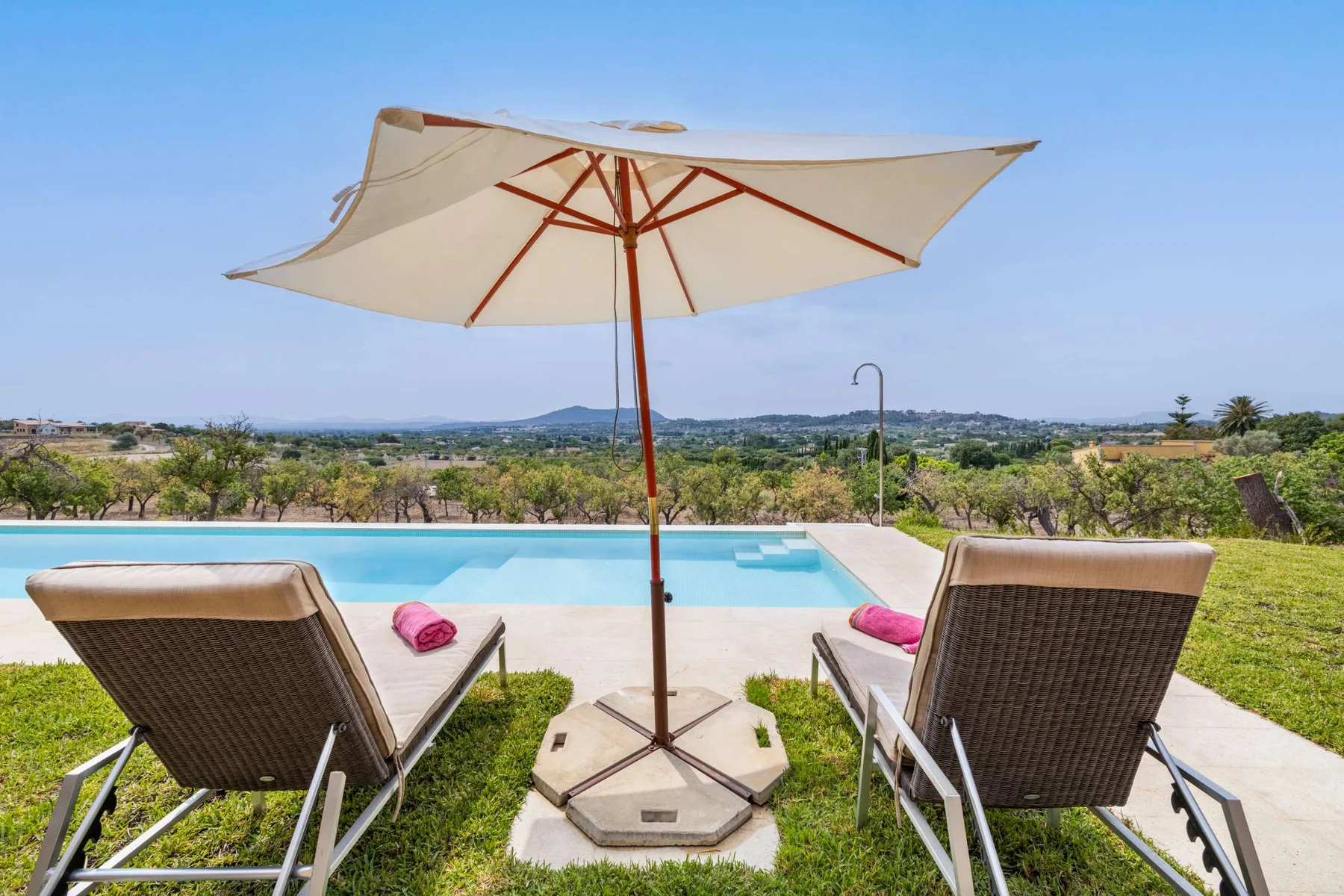 A swimming pool with lounge chairs sits beside a broad green landscape.