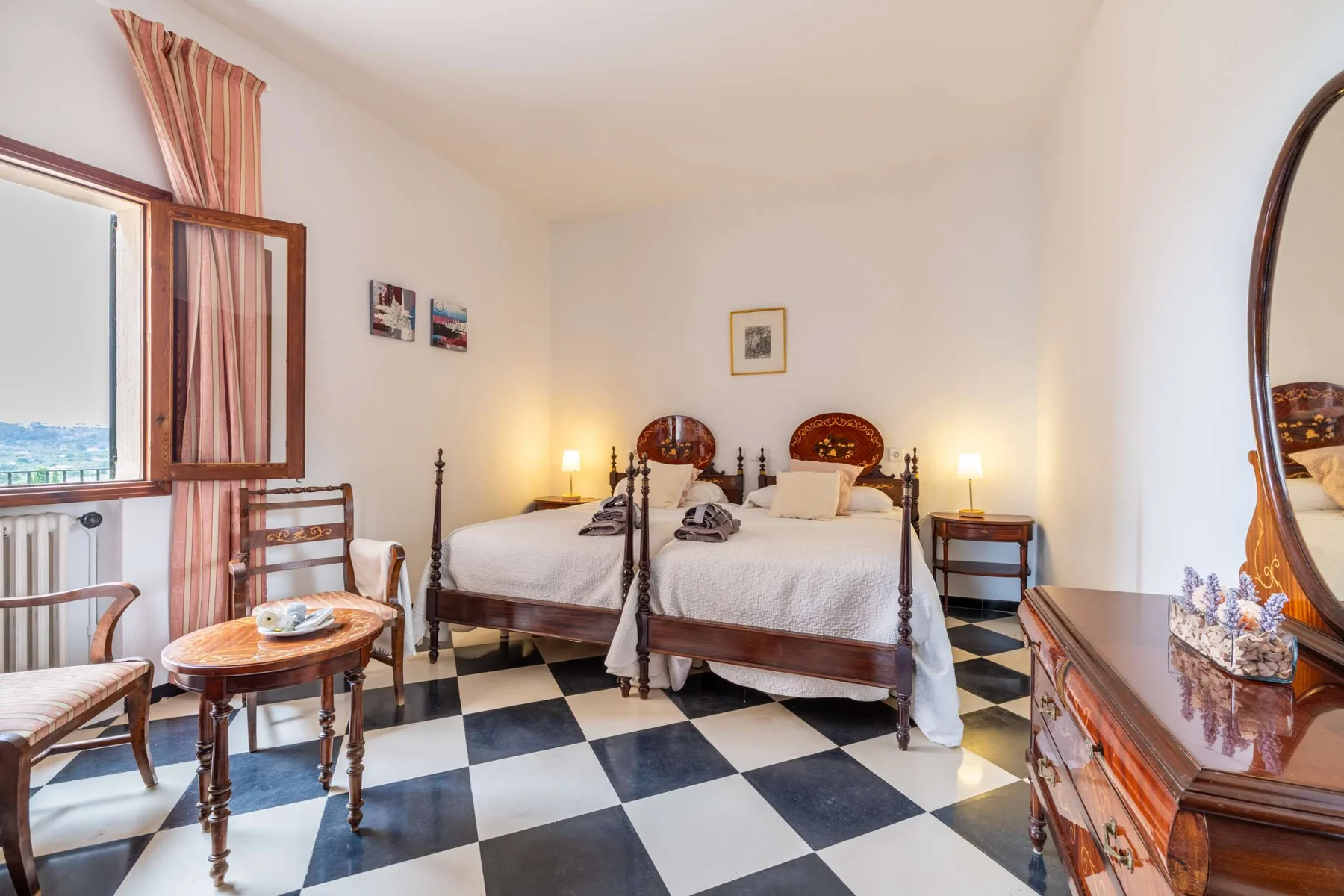 A bedroom with two beds, bedside tables, and a black-and-white checkered floor.