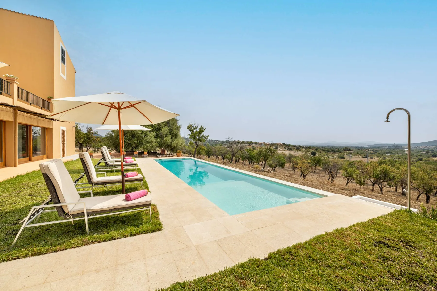 An outdoor swimming pool beside a house, with loungers and a broad countryside view.