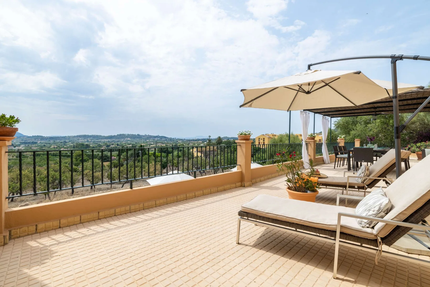 An outdoor terrace with lounge seating, a large umbrella, and a view across the hills.