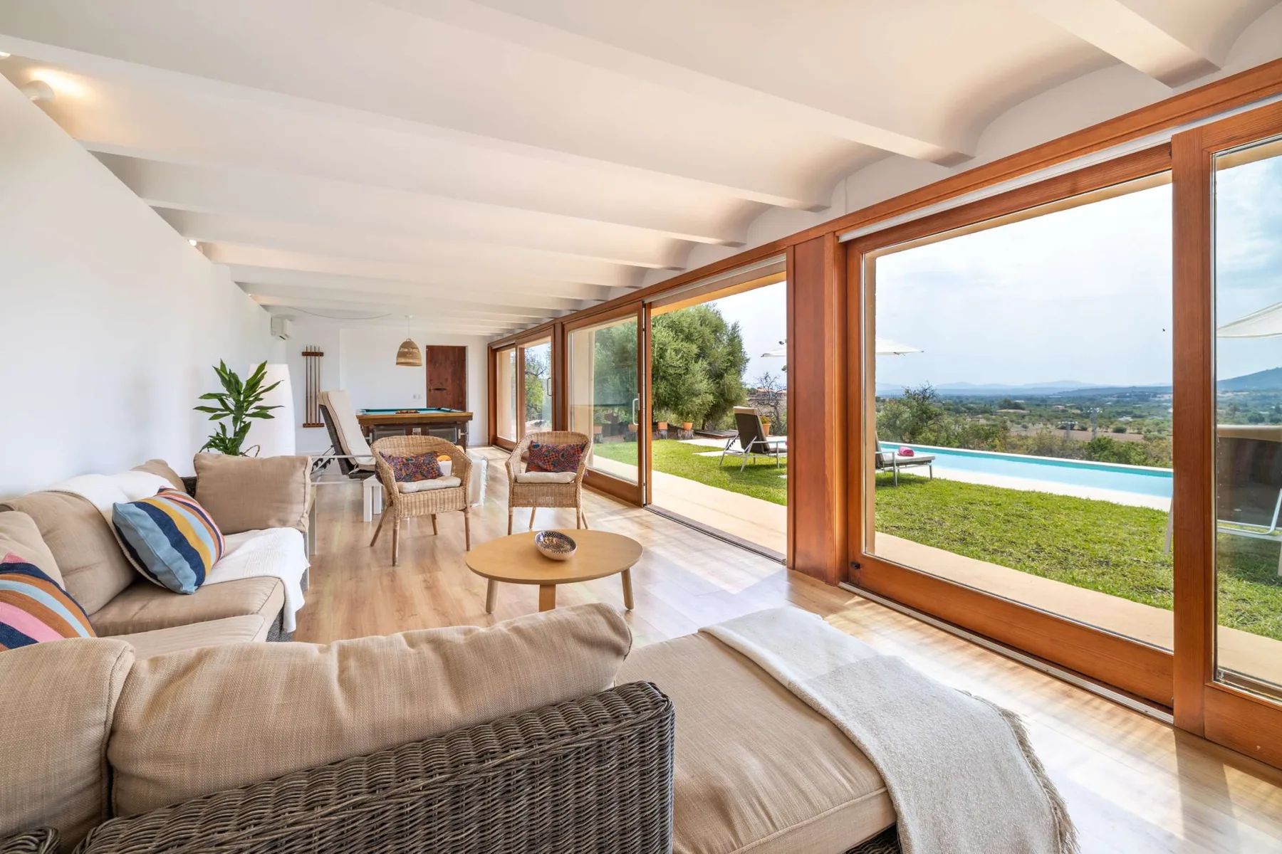 A bright living room opens onto a lawn and swimming pool through large windows.