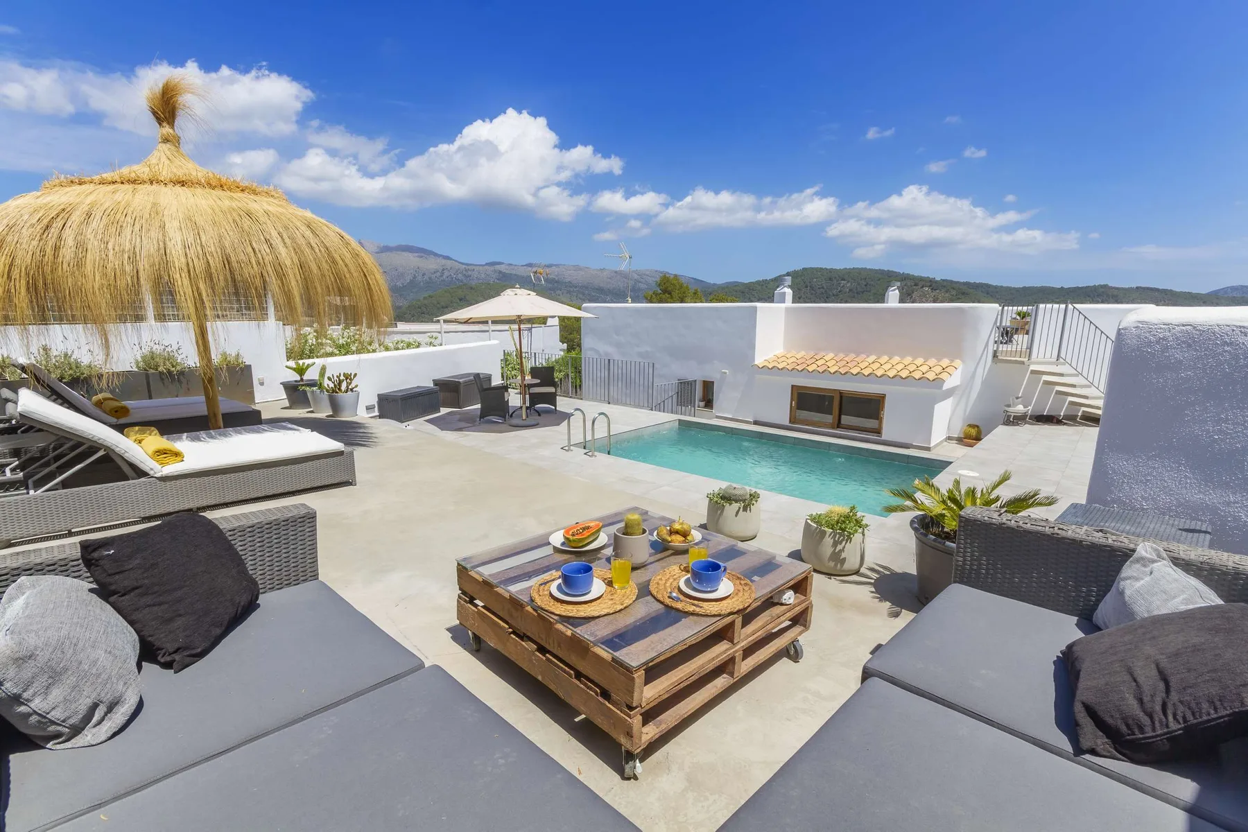 A sunny rooftop pool terrace with cushioned seating and a low table.