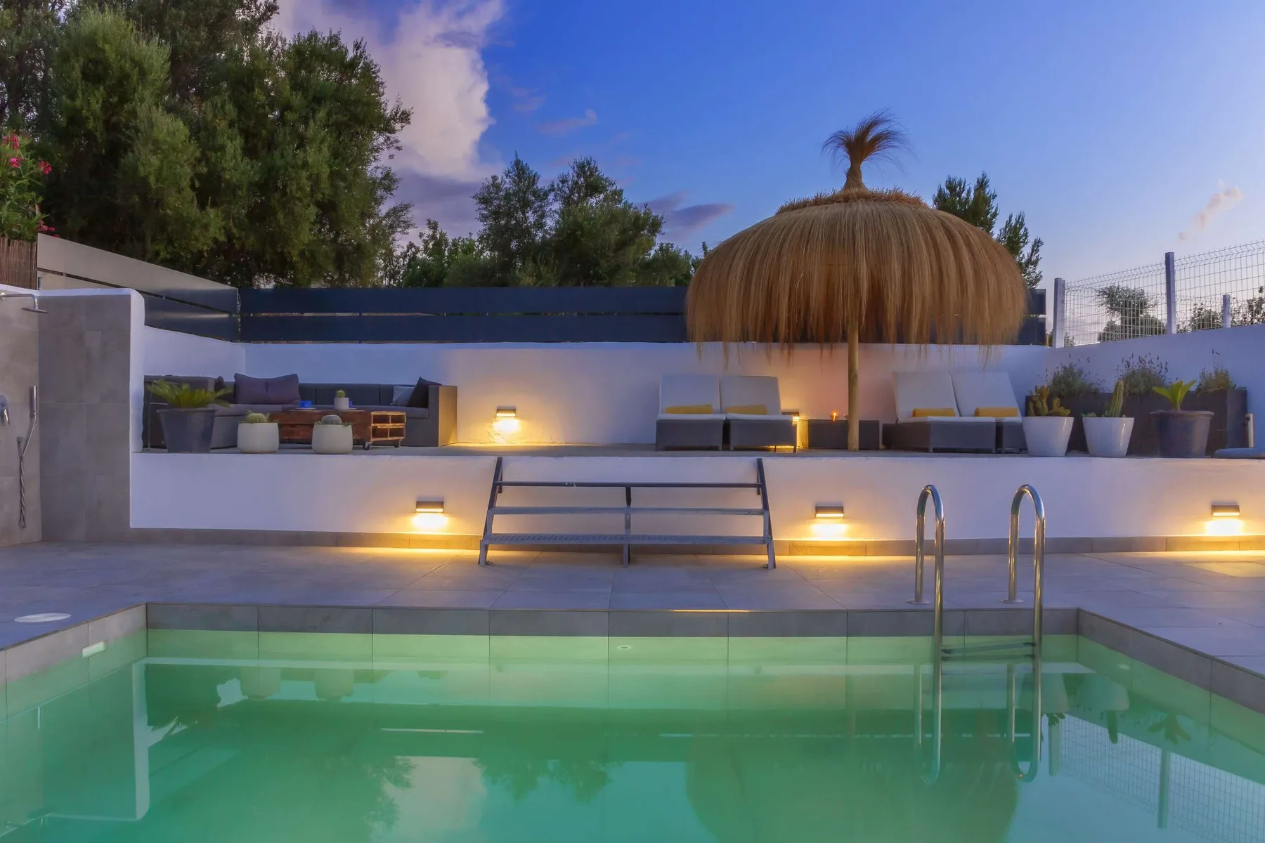 An outdoor swimming pool sits below a raised seating area at dusk.
