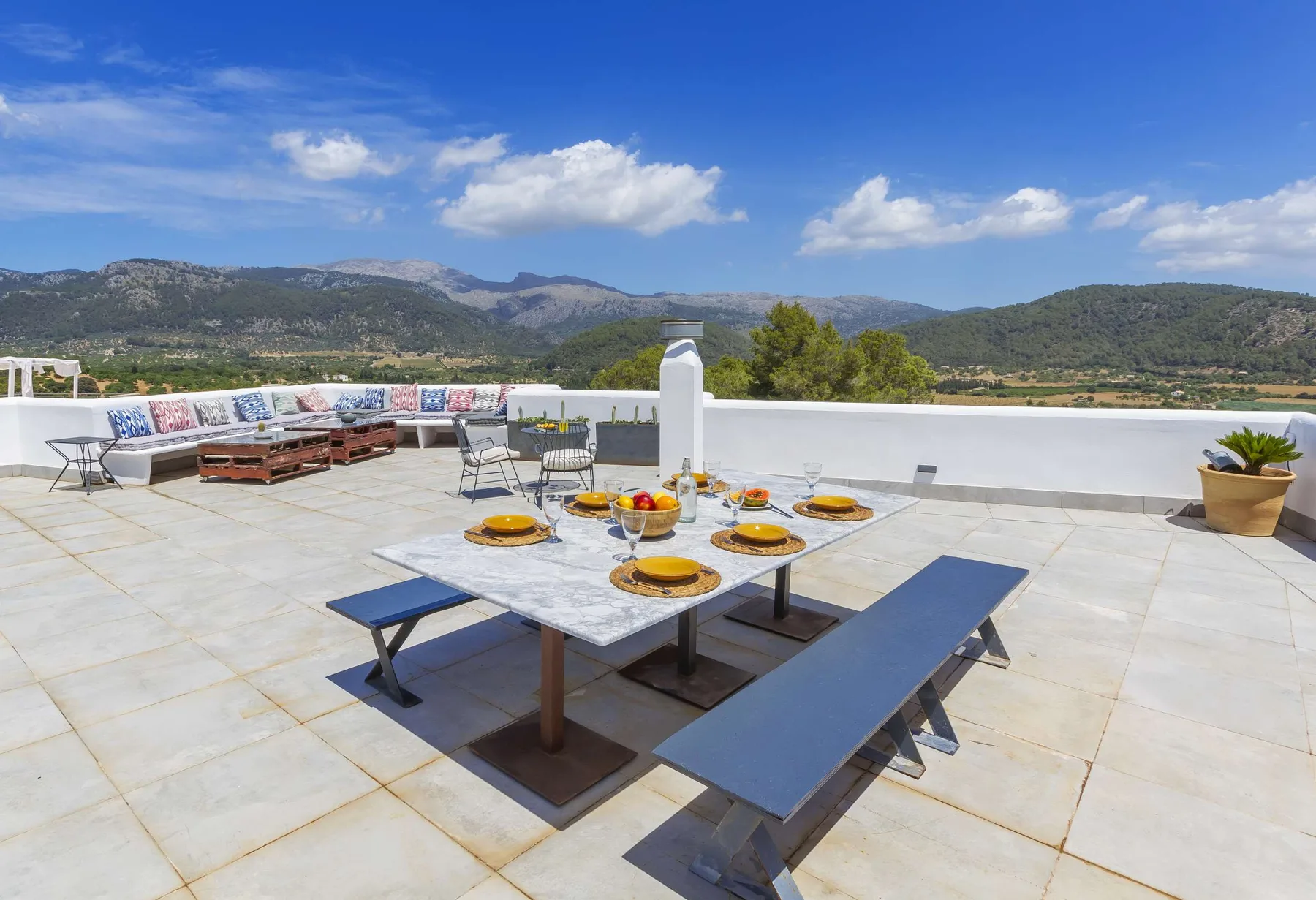 A rooftop terrace has a dining table and seating overlooking a mountain landscape.
