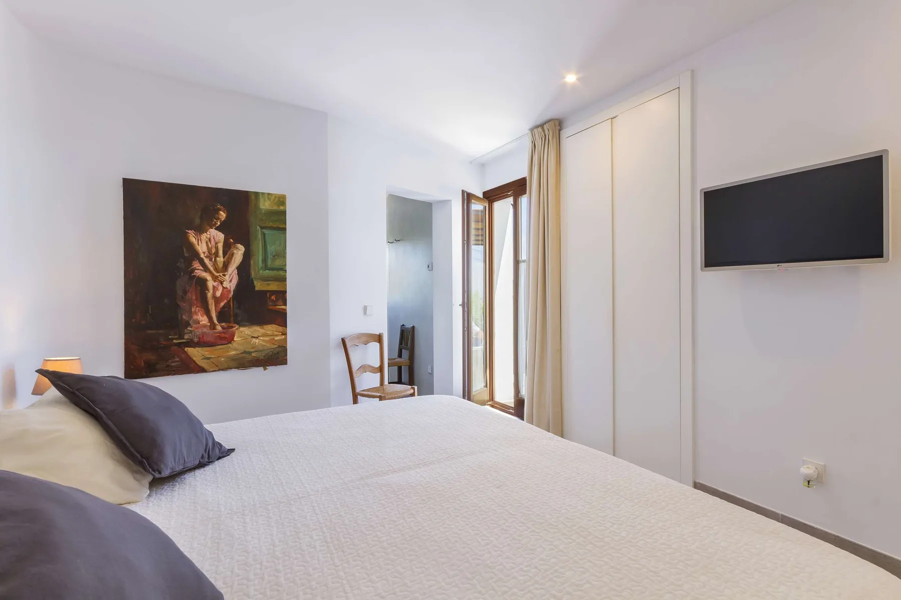 A bedroom with a neatly made bed, wall art, and a mounted television.