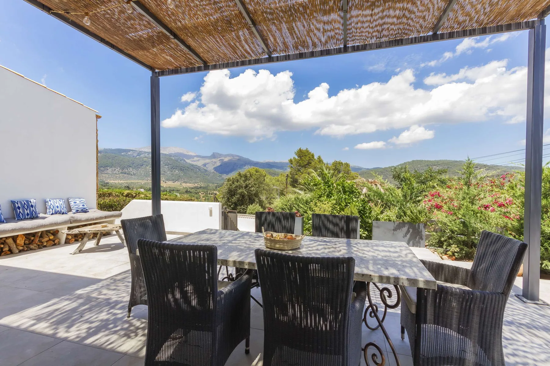 A shaded outdoor dining area overlooks green hills and a mountain range.