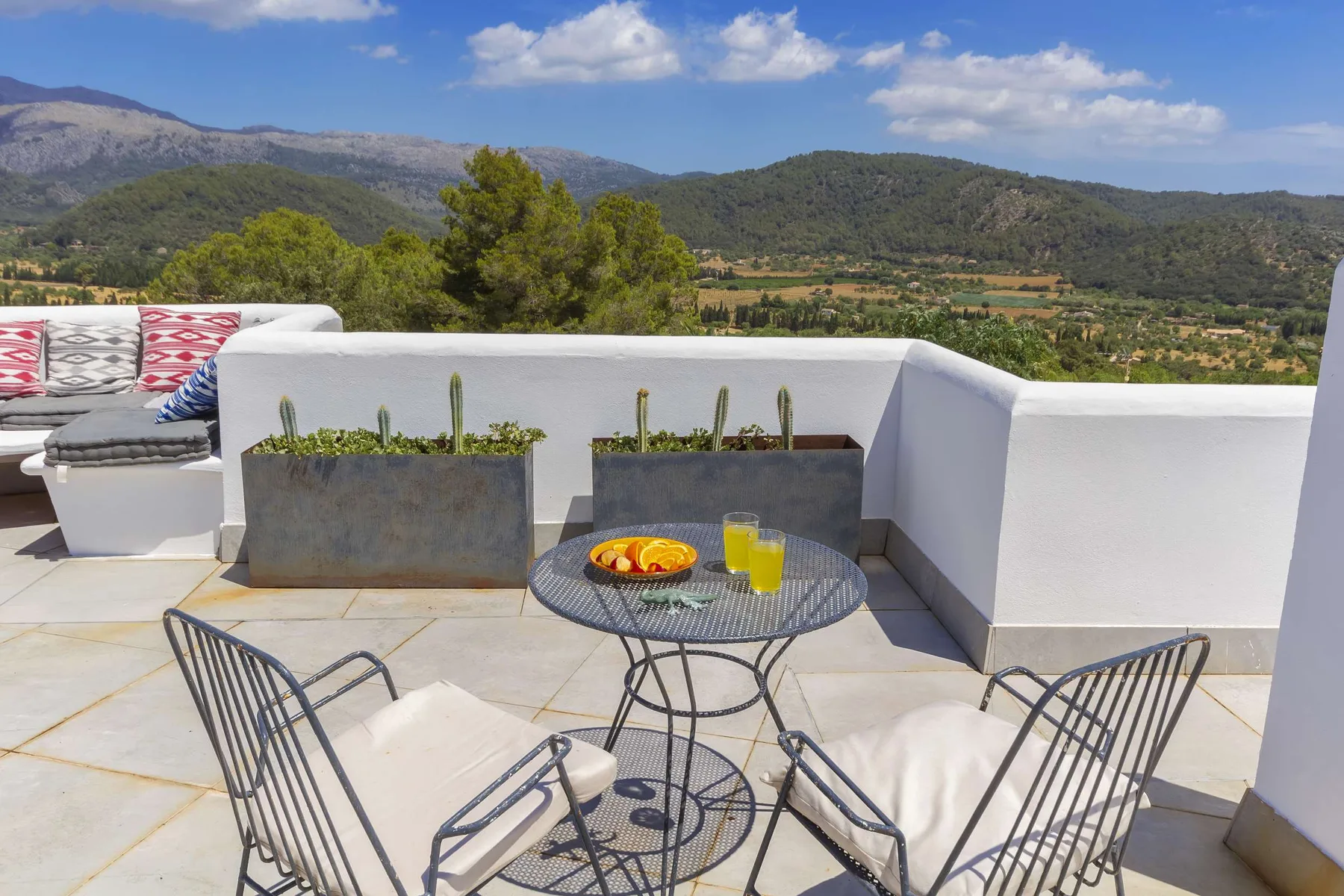 A rooftop patio has a round table and seating overlooking green hills.