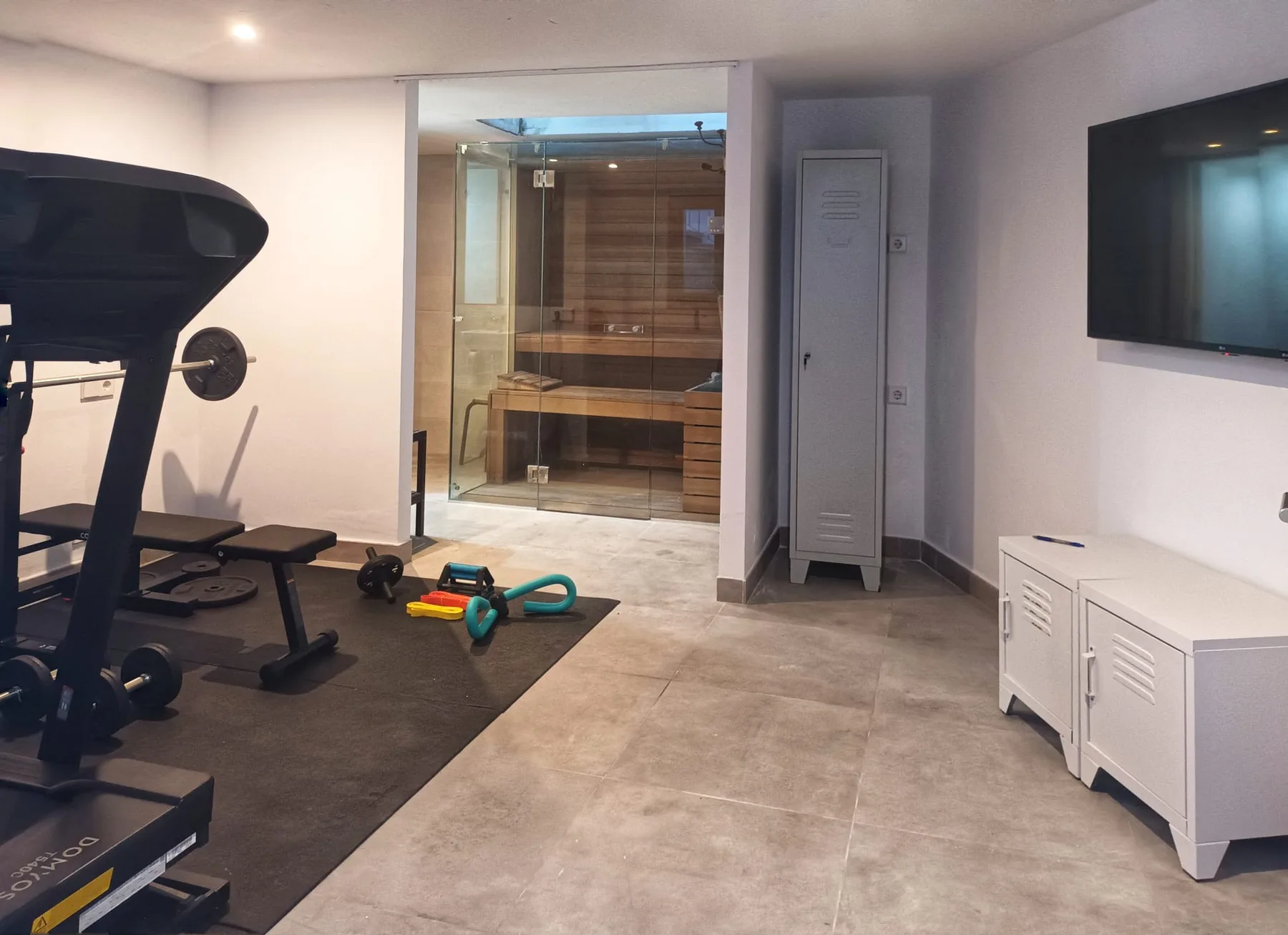 A home gym with exercise equipment and a glass-fronted sauna.